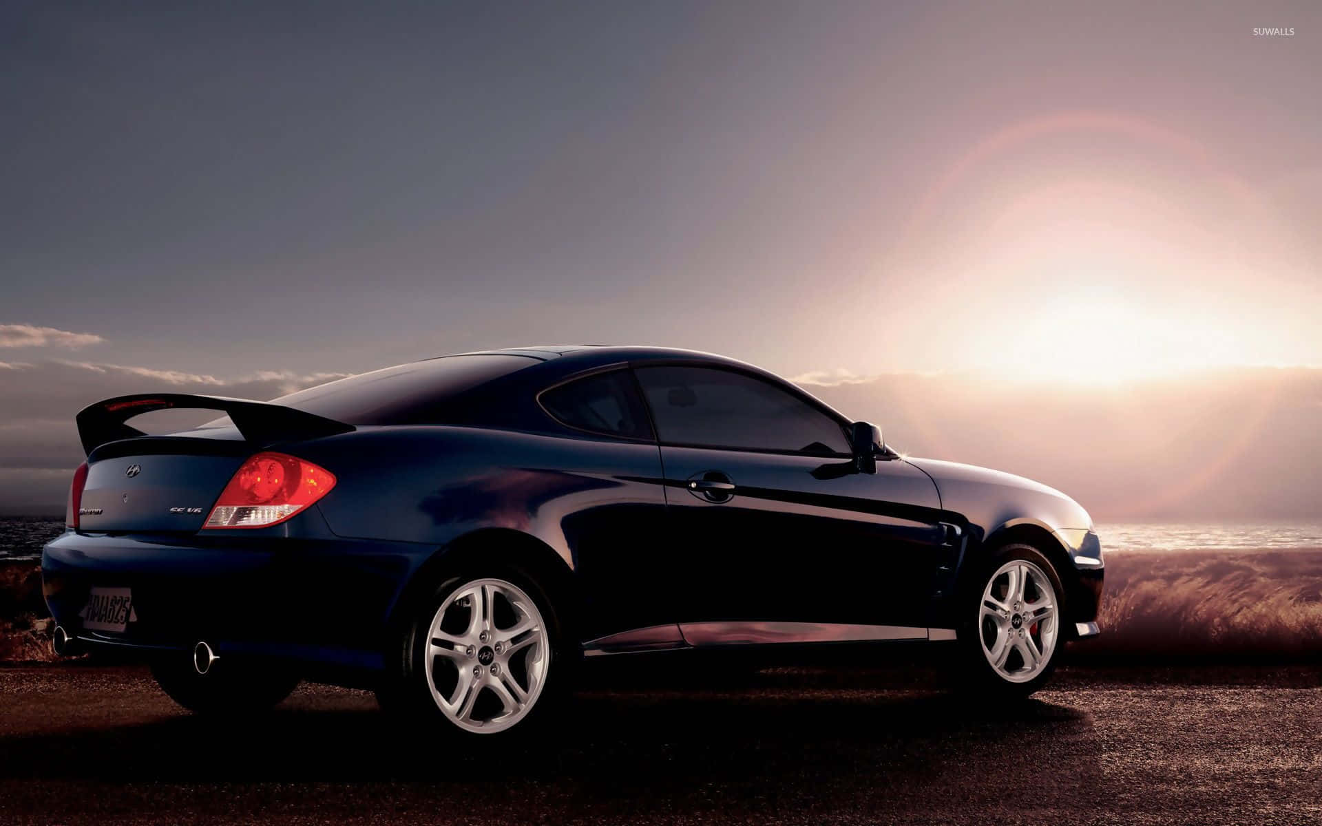 Hyundai Tiburon 桌布 壁紙 — 一輛時尚的黑色跑車在溫暖的日落天空下閃耀，鏡頭光暈和金色光線反射在其曲線上。