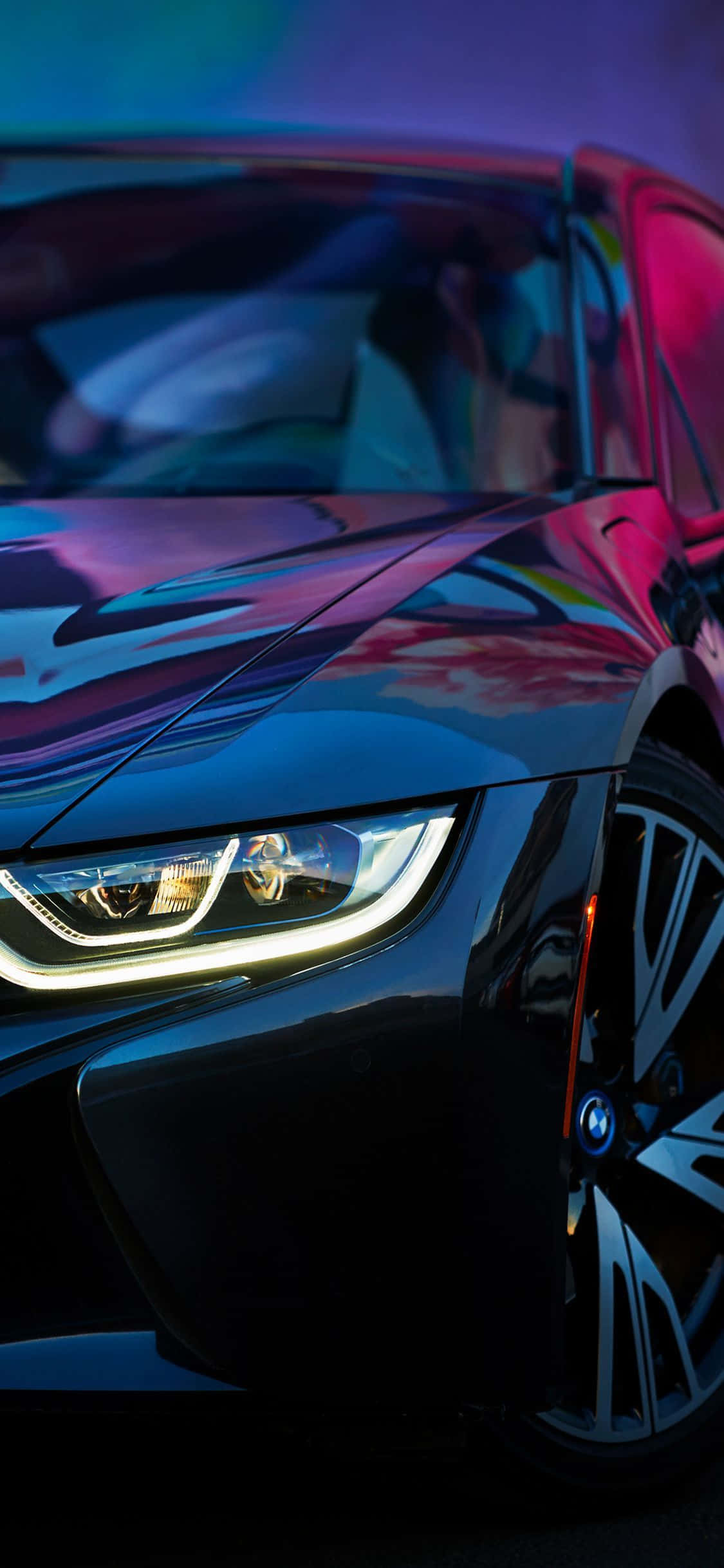 Bmw iPhone 桌布 壁紙 — 一輛時尚的黑色跑車在霓虹燈下閃耀，其光滑表面反射出鮮豔的紫色和粉紅色光芒。