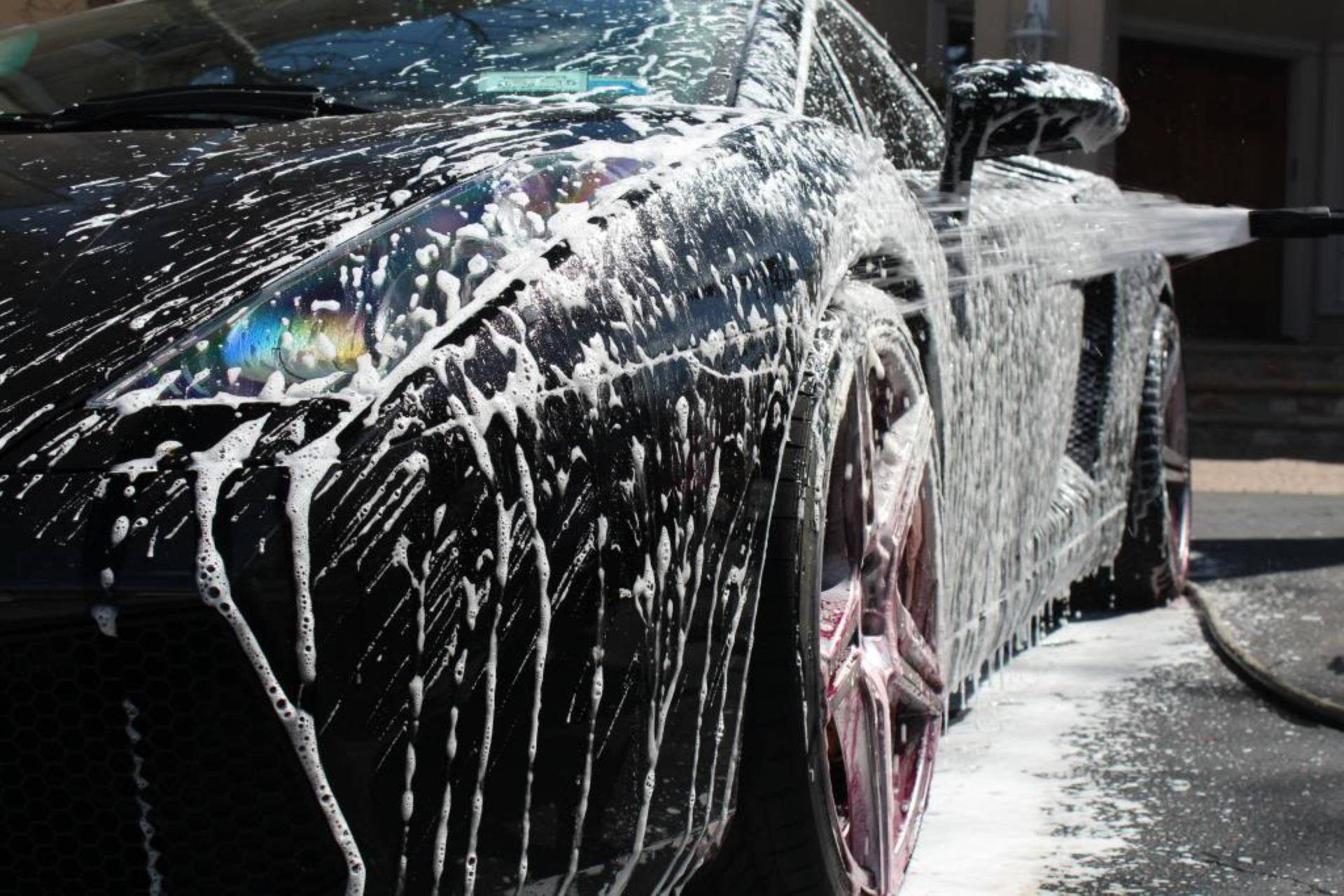 Wash 桌布 壁紙 — 一輛時尚的黑色跑車覆蓋著厚厚的白色肥皂泡，正在明亮的陽光下進行高壓清洗。
