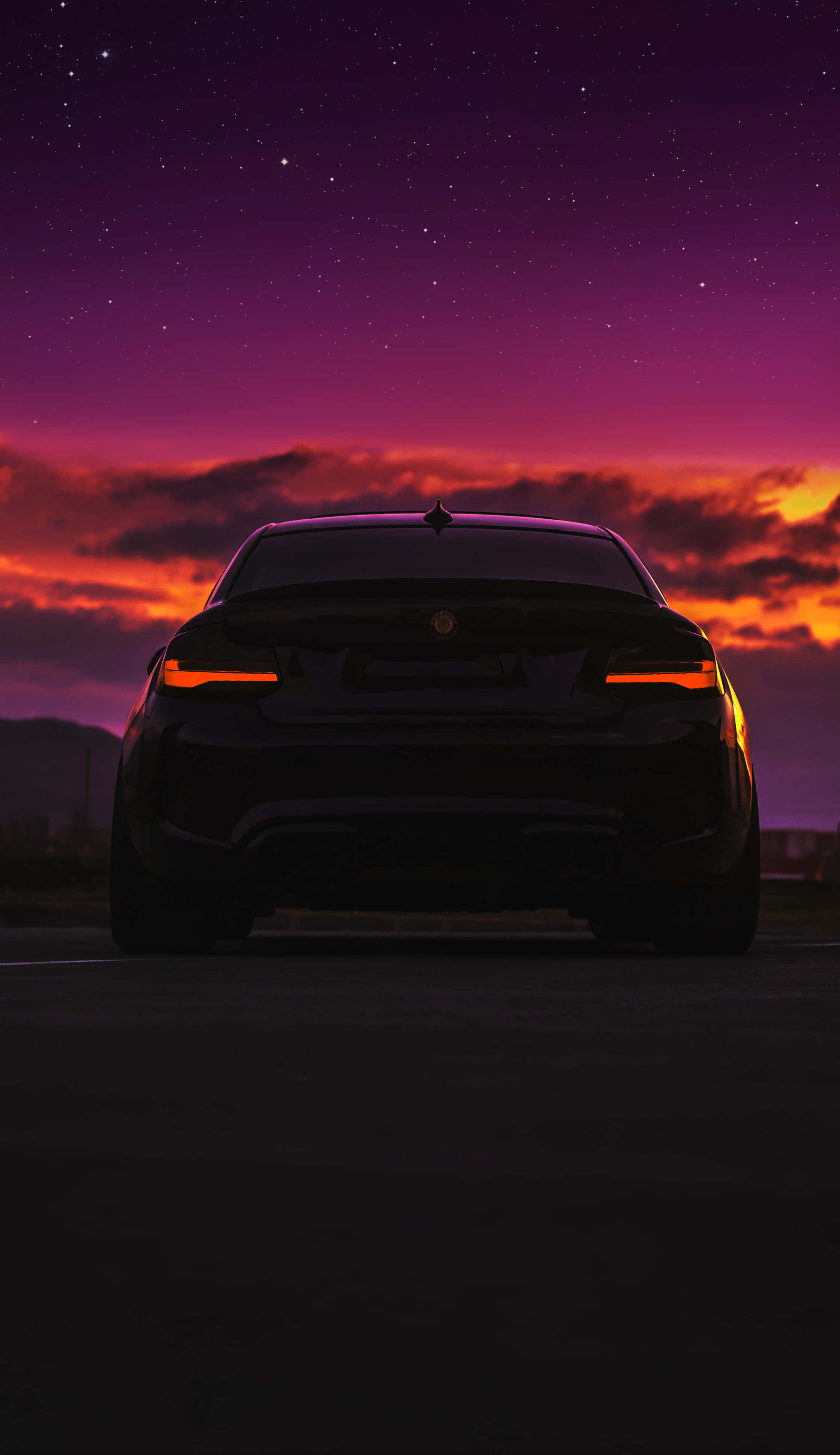 Best M Series 桌布 壁紙 — 一輛時尚的黑色跑車輪廓在充滿活力的紫色和橙色星空暮色天空下，散發著橙色的尾燈光芒。
