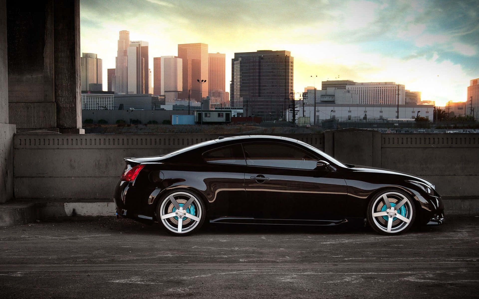 Infiniti G35 桌布 壁紙 — 一輛時尚的黑色跑車配備發光藍色煞車，停在一座橋下，背景是金色日落城市天際線。