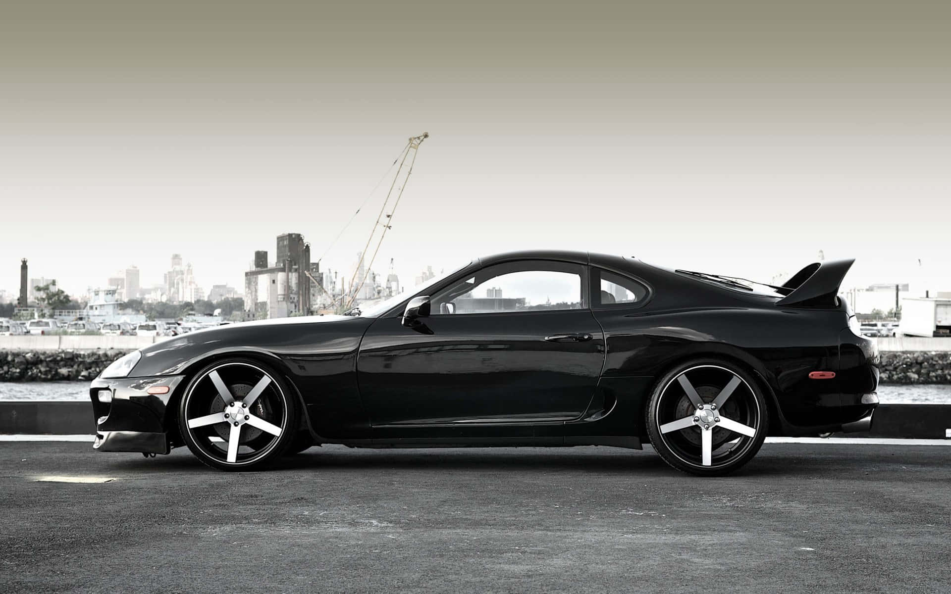 黑色跑車停在海濱，背景是城市天際線。 — Toyota Supra Mk4 壁紙