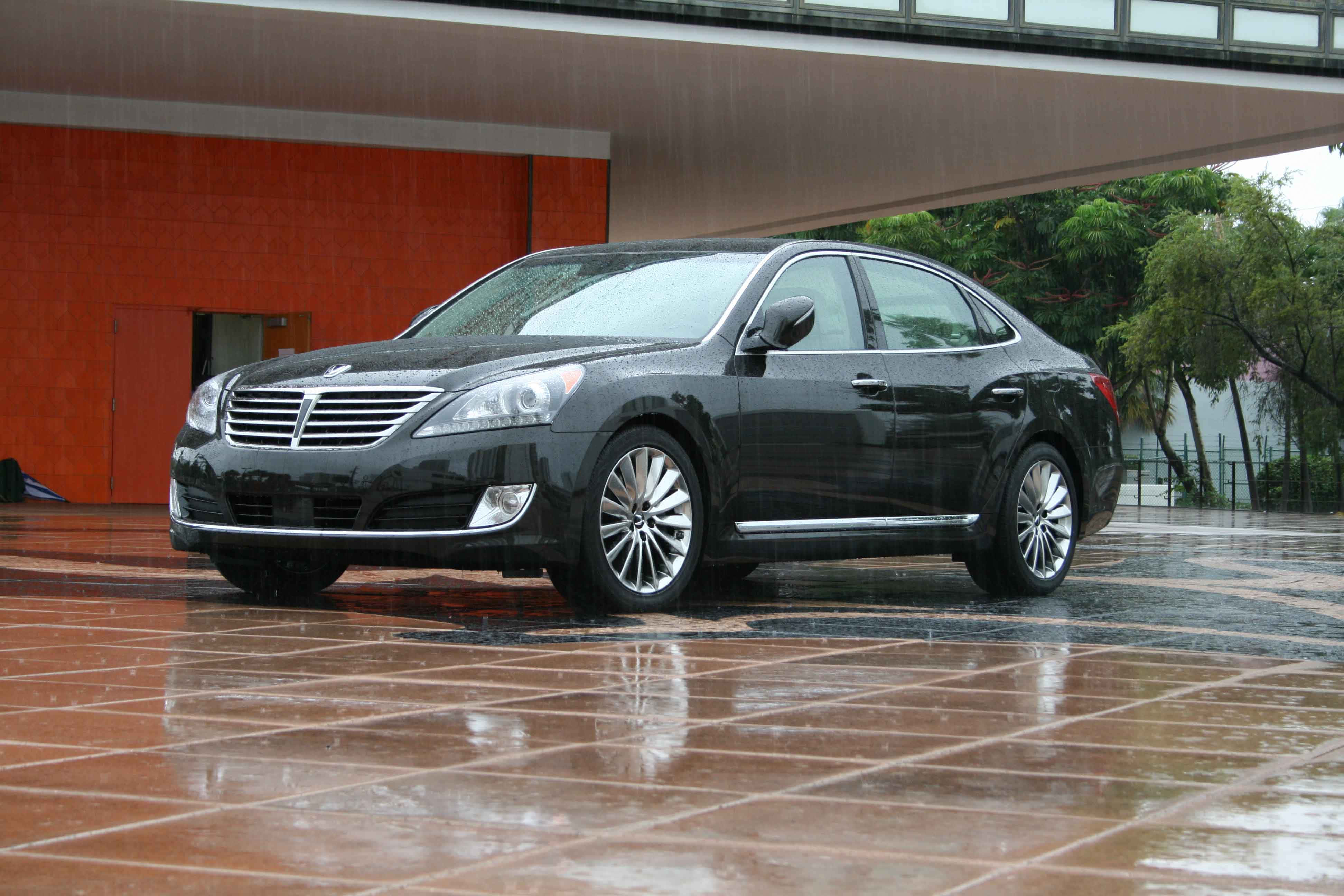 Hyundai Equus 桌布 壁紙 — 一輛時尚的黑色轎車在現代建築懸挑下的濕瓷磚廣場上，在雨滴下閃閃發光。