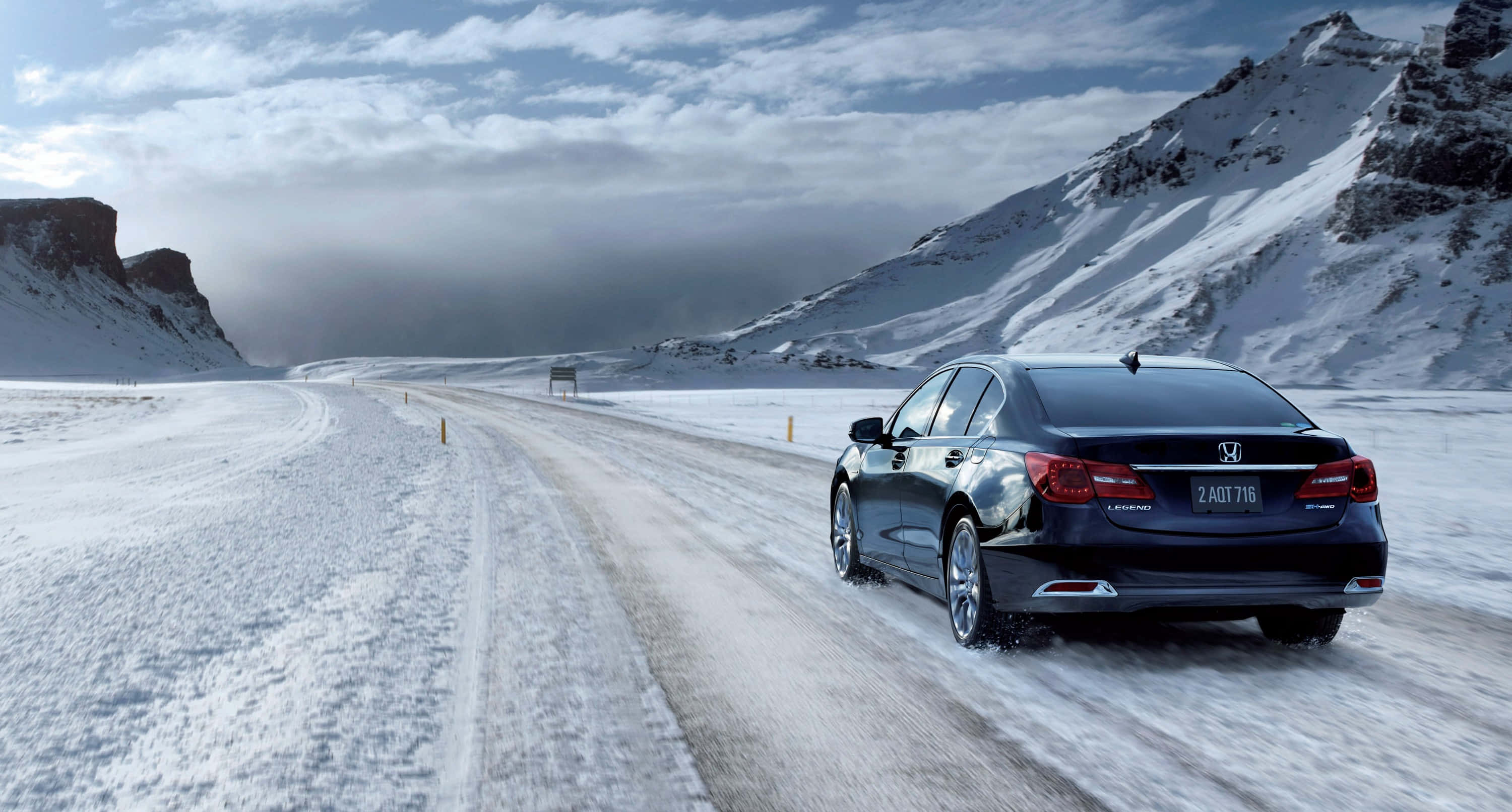 Honda Legend 桌布 壁紙 — 一輛時尚的黑色轎車在積雪的道路上行駛，兩旁是高聳的冰山，天空多雲。