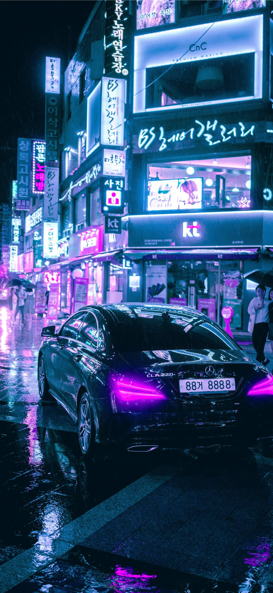 手機 桌布 壁紙 — 一輛時尚的黑色轎車在雨濕的韓國街道上，霓虹燈下閃耀，反射出鮮豔的紫色和藍色。