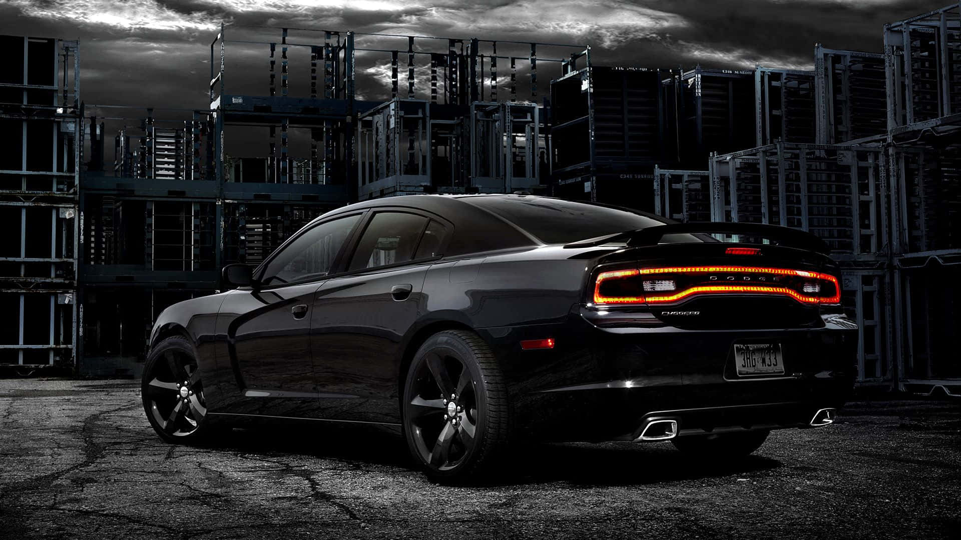Dodge Charger 桌布 壁紙 — 一輛時尚的黑色道奇Charger，帶有發光的橙色尾燈，停放在暴風雨天空下粗糙的工業場地中。