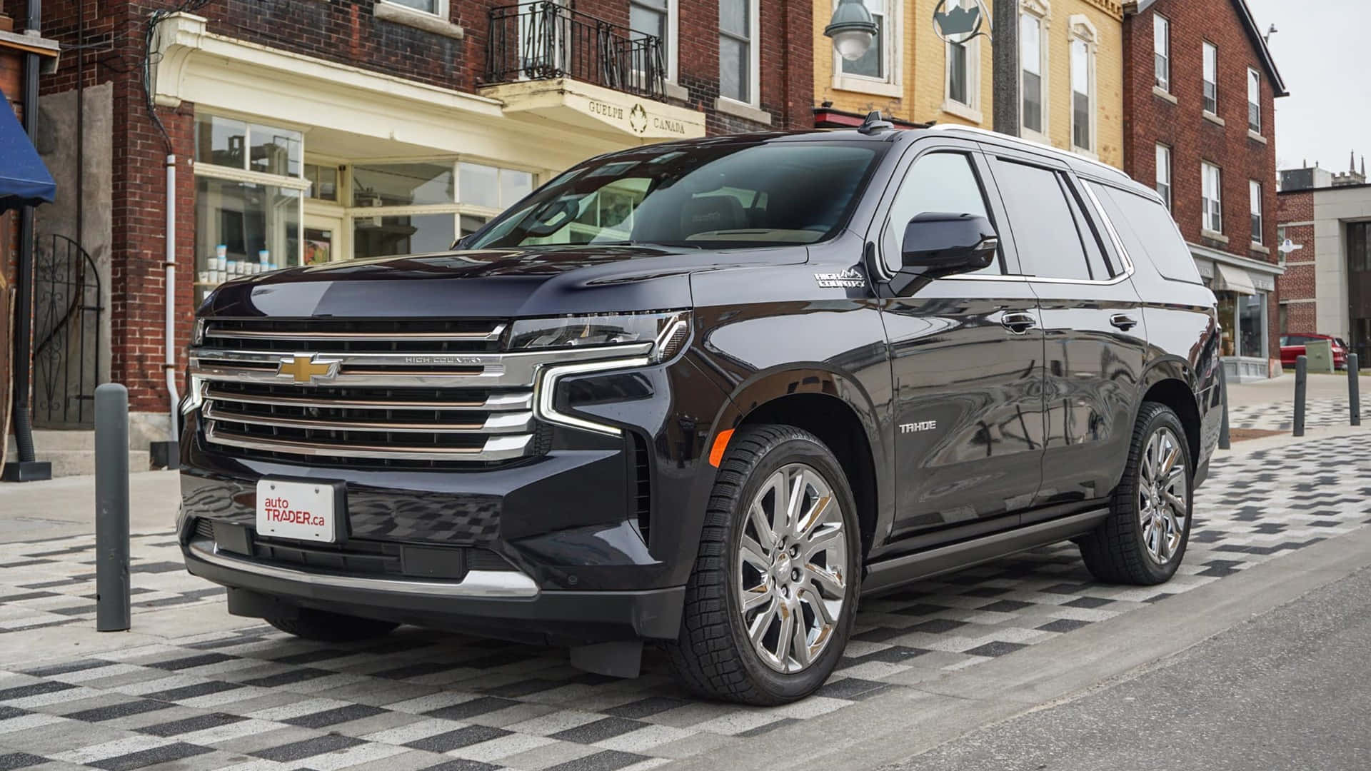 Chevrolet 桌布 壁紙 — 一輛時尚的黑色雪佛蘭 Tahoe SUV 停放在磚砌建築前的棋盤格人行道上。