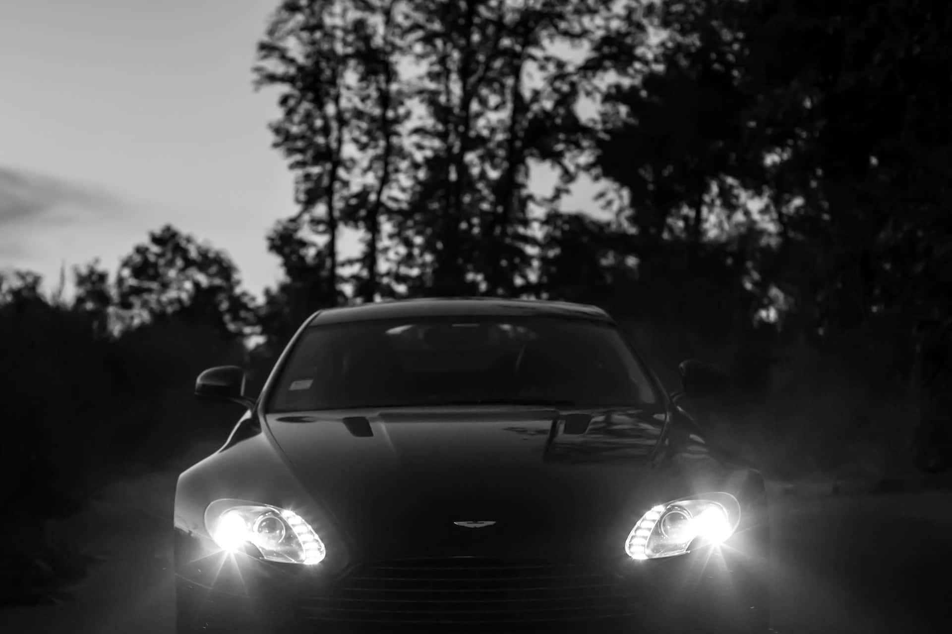 Black And White Car 桌布 壁紙 — 一輛時尚跑車閃爍車頭燈，在暮色中穿過迷霧森林，呈現單色調。