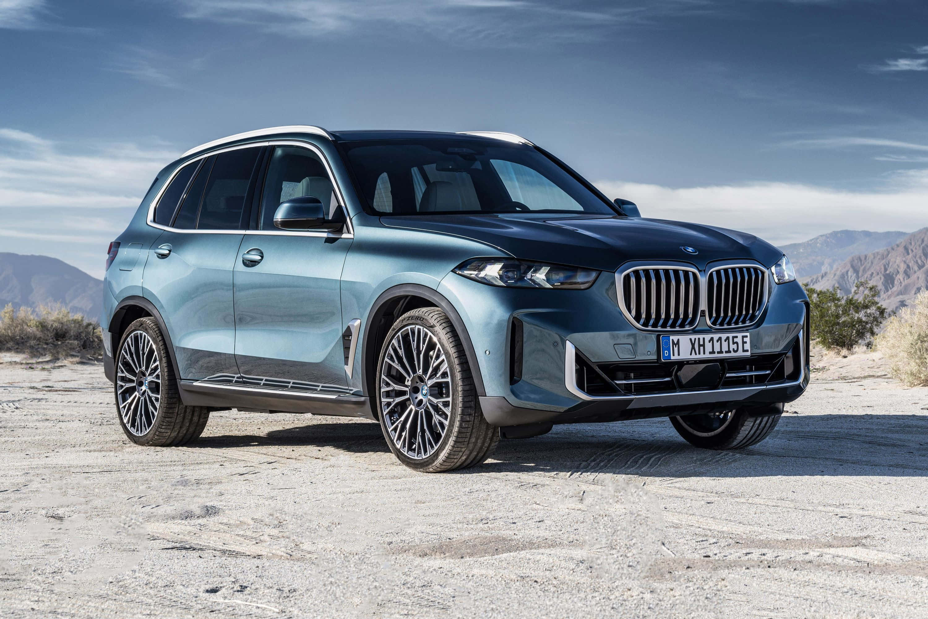 Bmw X5 桌布 壁紙 — 一輛時尚金屬藍色BMW X5 SUV停在龜裂的沙漠路面上，遠山在望，天空局部多雲。