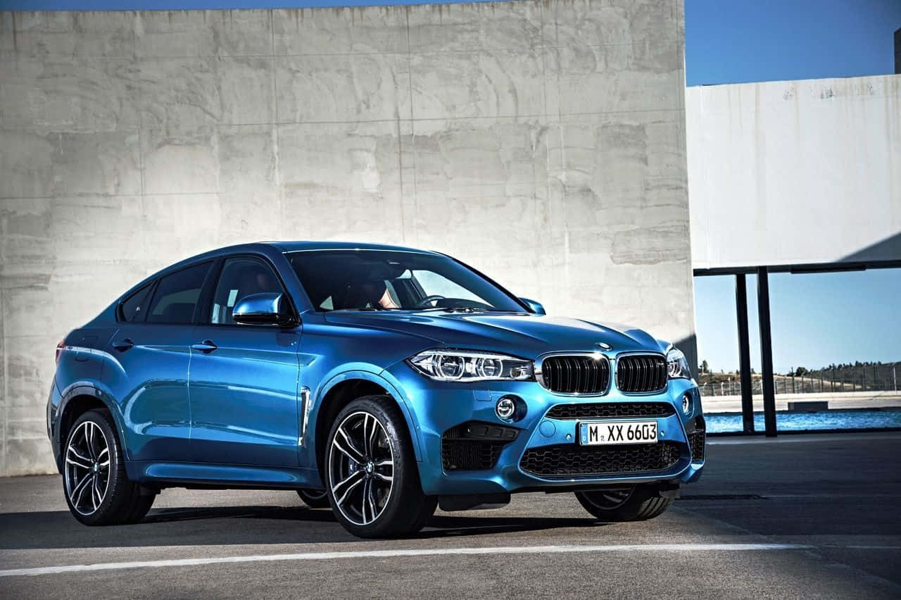 Bmw X6 桌布 壁紙 — 一輛時尚金屬藍色BMW X6 M在明亮日光下停放在簡約混凝土牆旁。