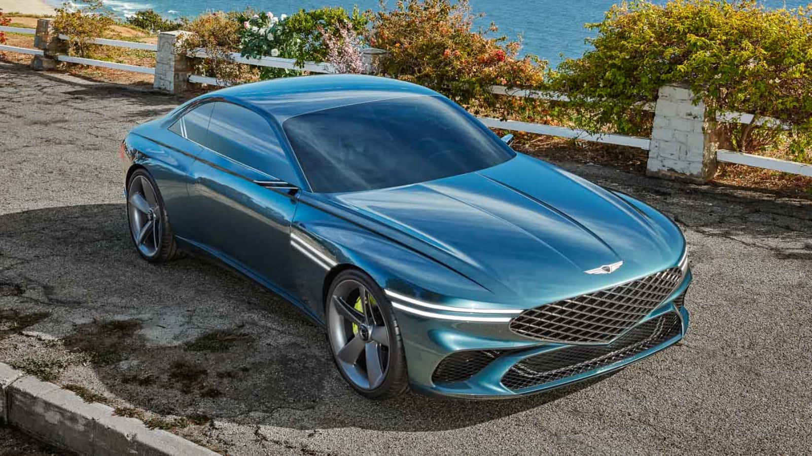 Genesis 桌布 壁紙 — 一輛時尚金屬藍色跑車停泊在沿海公路上，背景有海洋和綠植。