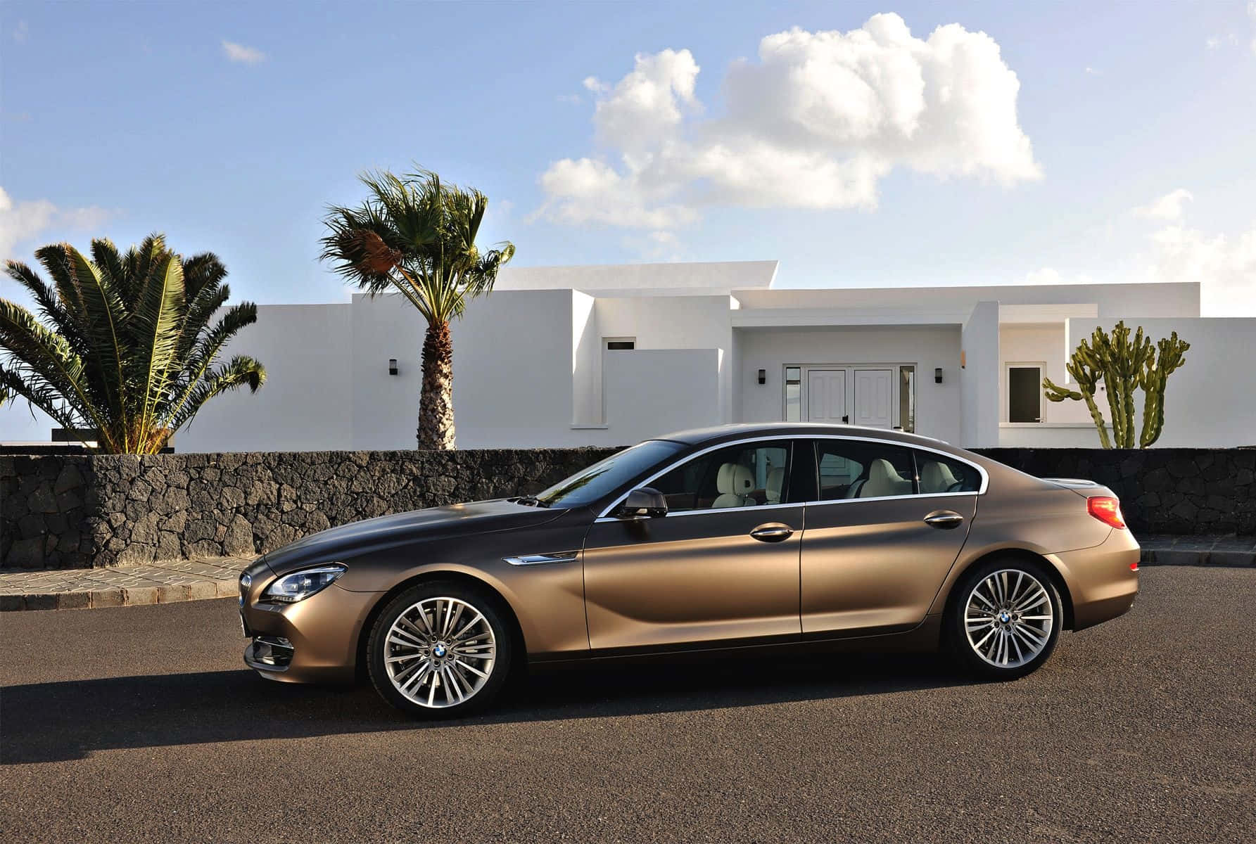 Bmw 6 Series 桌布 壁紙 — 一輛時尚金色寶馬轎車停在現代白色別墅前的柏油路上，別墅周圍有棕櫚樹，上方是明亮的藍天。