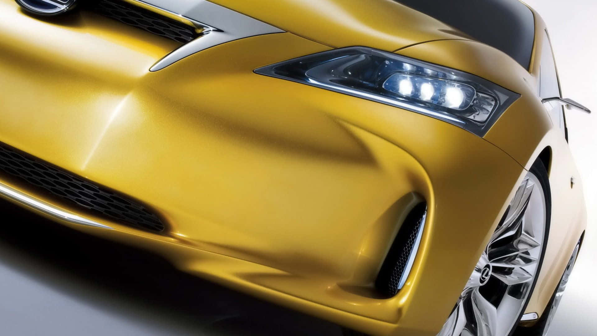 Yellow Car 桌布 壁紙 — 一輛時尚金色跑車前部的特寫，在乾淨的攝影棚背景下展示其銳利的前燈和空氣動力學曲線。