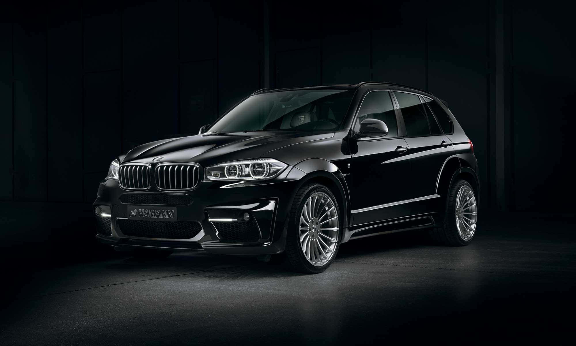 Bmw X5 桌布 壁紙 — 一輛時尚黑色 Hamann 改裝 BMW X5 SUV 在昏暗工業環境的戲劇性攝影棚燈光下閃耀。