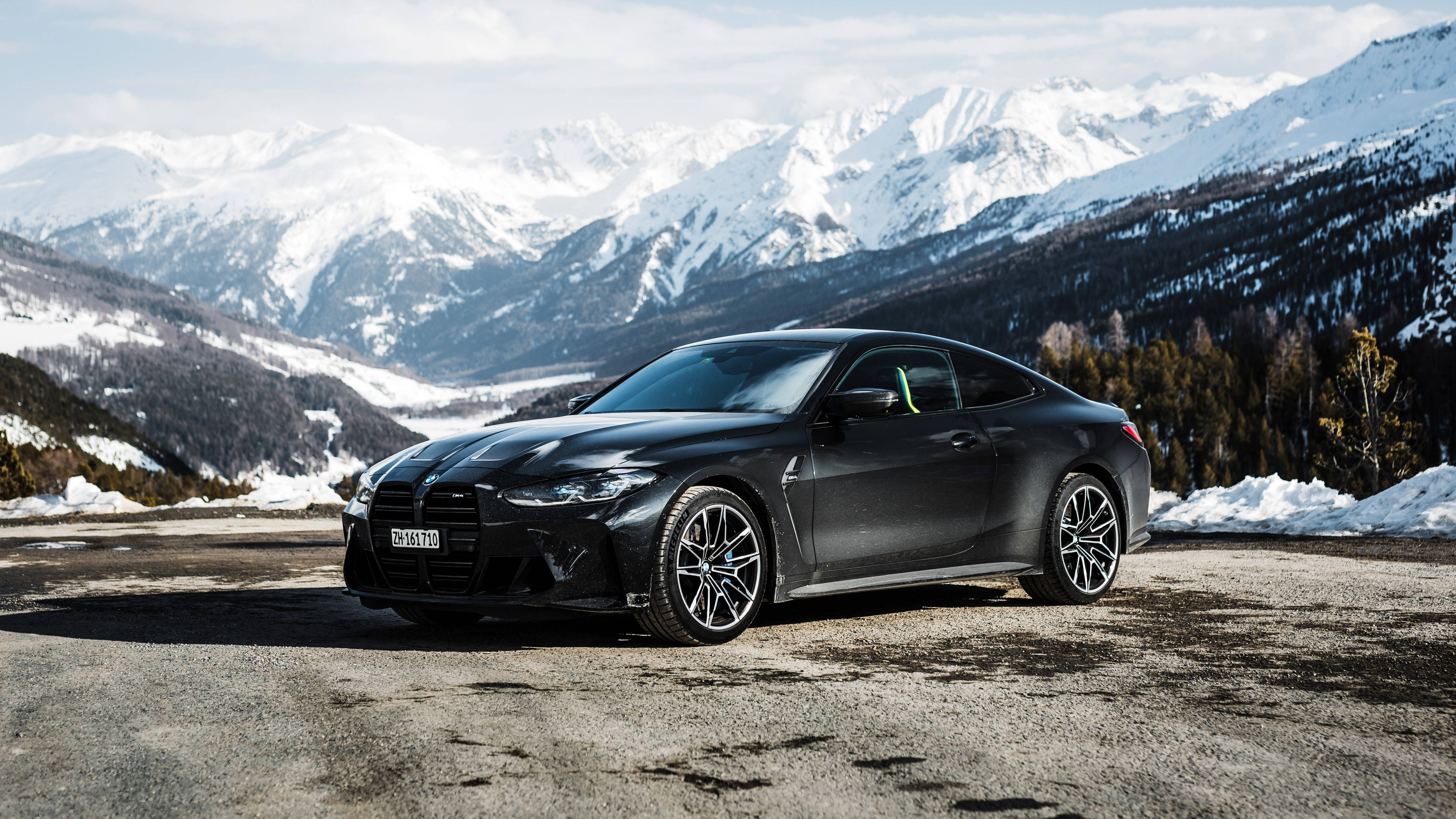 4K BMW 壁紙 桌布 壁紙 — 一輛時尚黑色BMW M4轎跑車停泊在積雪的山路上，背景是白雪覆蓋的山峰。