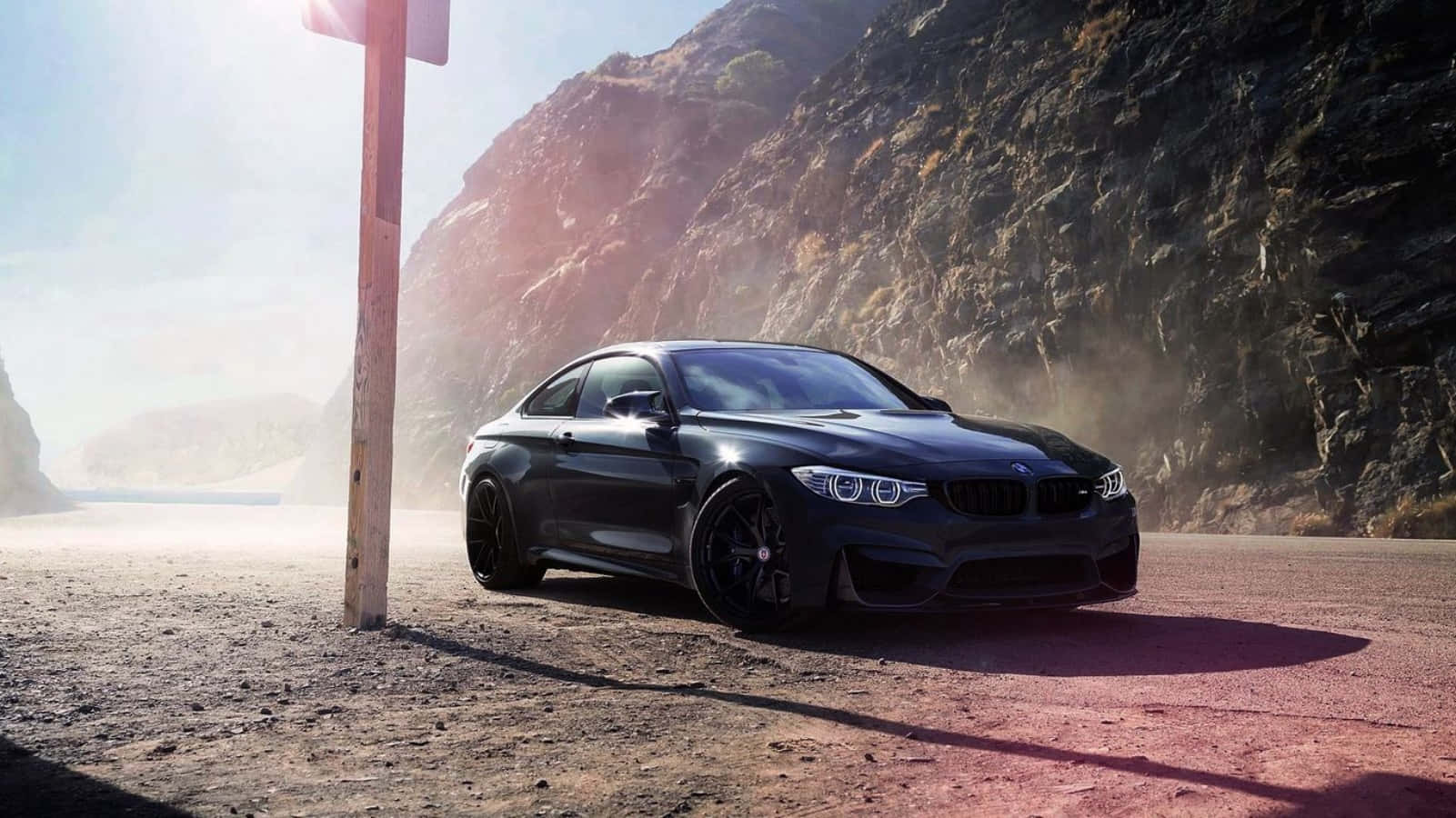Bmw Cars 桌布 壁紙 — 一輛時尚黑色BMW M4轎跑車停泊在塵土飛揚的路邊，背景是崎嶇的懸崖和太陽眩光。