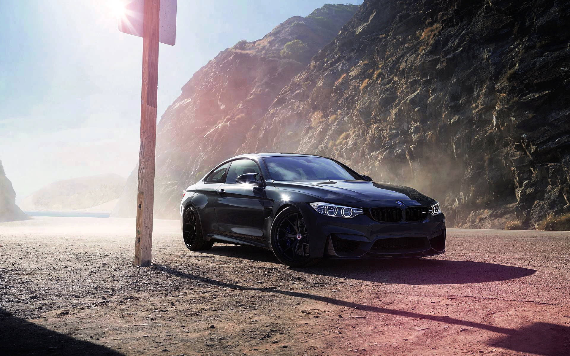 BMW 動圖 桌布 壁紙 — 一輛時尚黑色BMW M4雙門轎跑車停在塵土飛揚的路邊，背後是岩石懸崖和明亮的太陽耀斑。