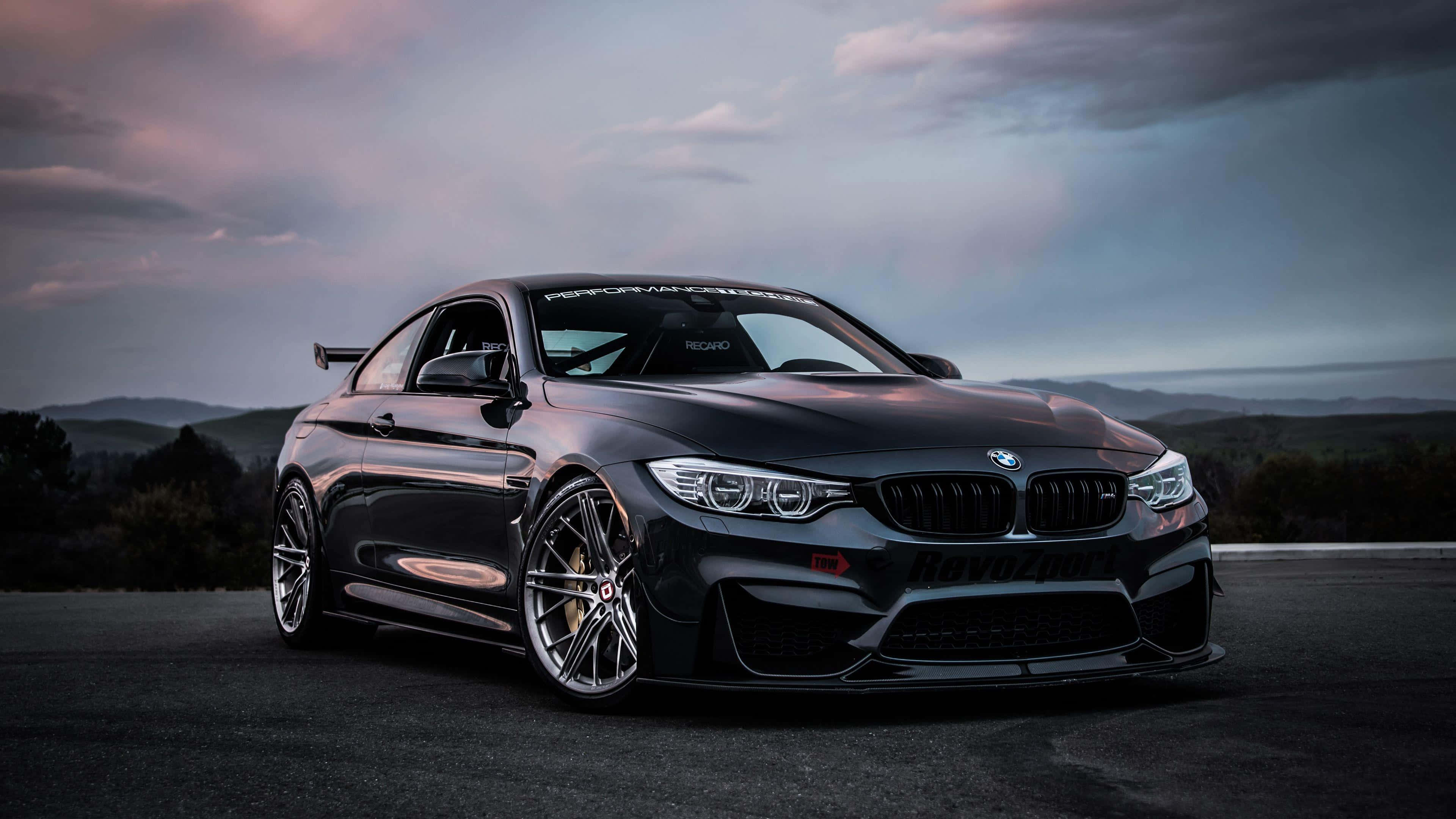 4K BMW 壁紙 桌布 壁紙 — 一輛時尚黑色BMW M4雙門轎跑車，配備訂製輪圈和後擾流板，停放在黃昏時的柏油路上，背景有山巒。