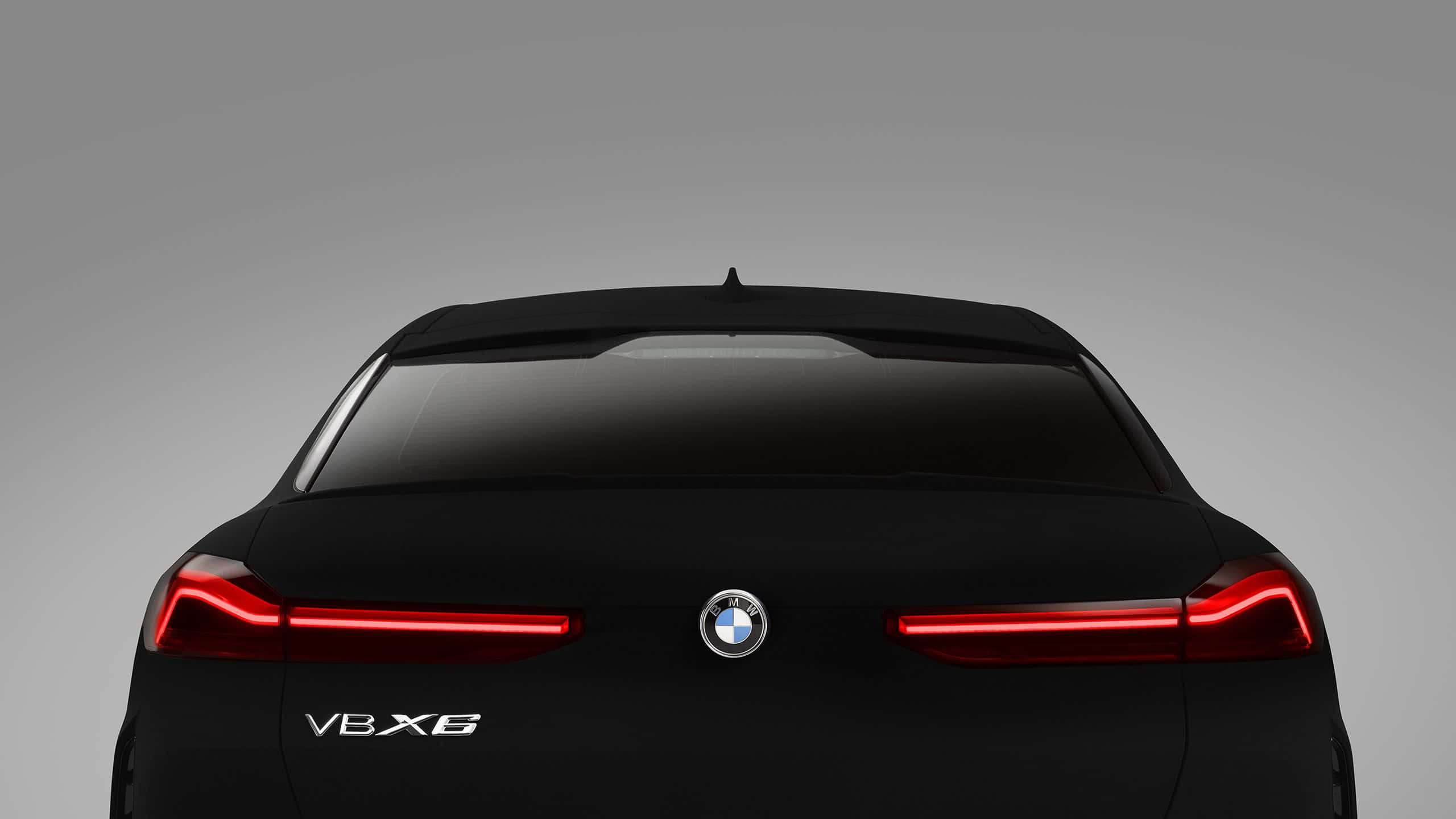 Vantablack 桌布 壁紙 — 一輛時尚黑色BMW V8X6的後視圖，紅色尾燈發光，背景為中性灰色。