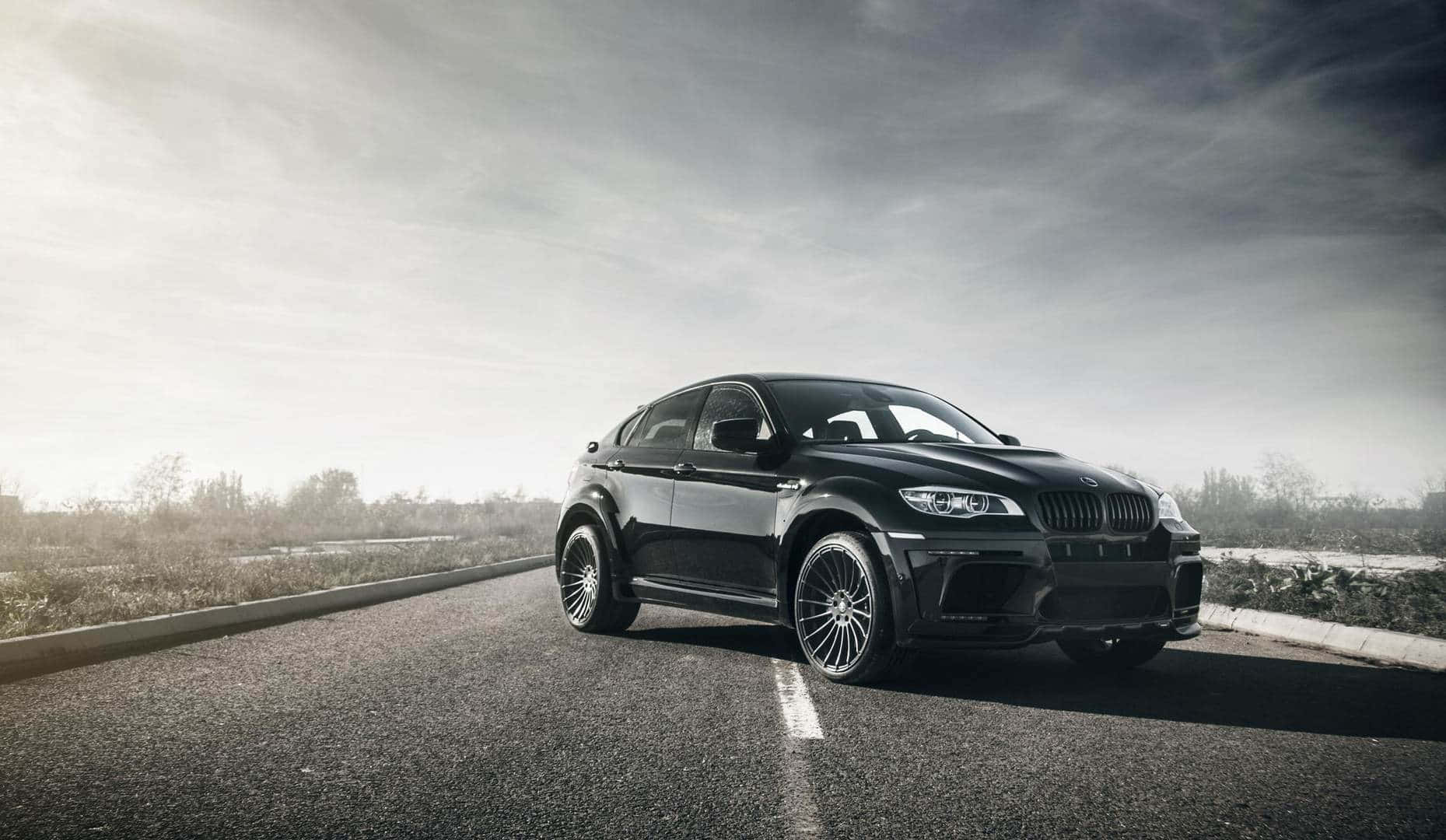 BMW X6 M 桌布 壁紙 — 一輛時尚黑色BMW X6 M跑車停放在陰天下空無一人的瀝青道路上。