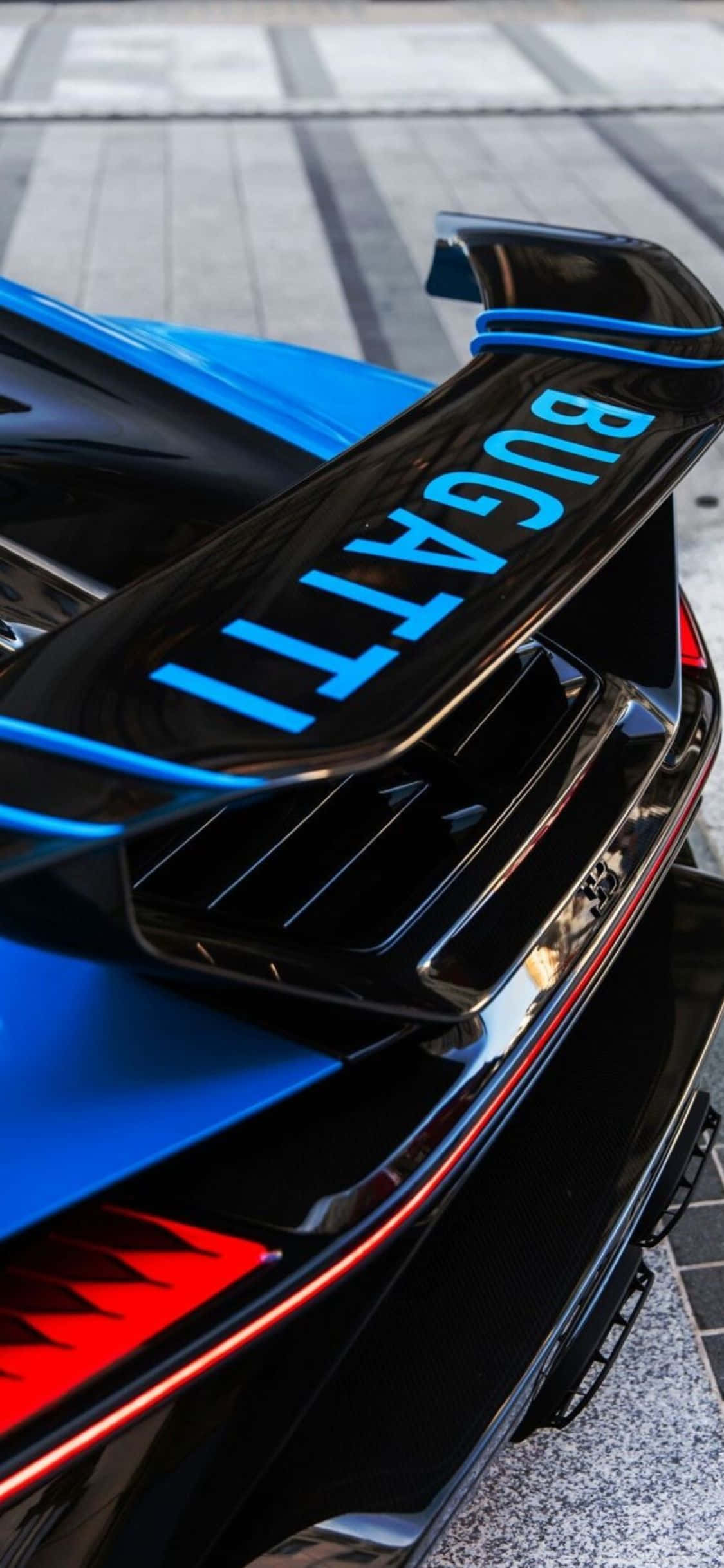 iPhone Xs Bugatti 桌布 壁紙 — 一輛時尚黑色Bugatti超級跑車的近距離特寫，帶有發光藍色點綴和紅色細節，停在鋪砌路面上。
