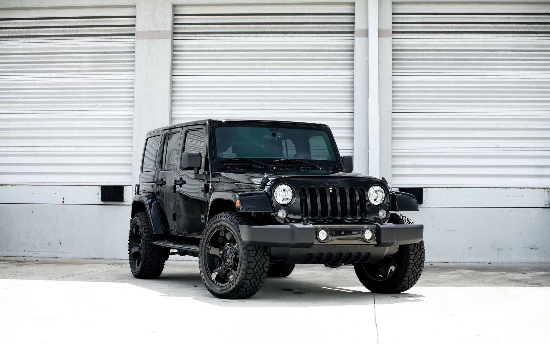 黑色吉普車 桌布 壁紙 — 一輛時尚黑色Jeep Wrangler在明亮日光下，停放在白色工業車庫門前。