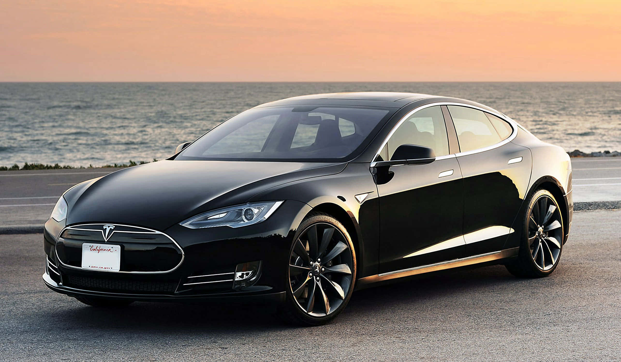 特斯拉 桌布 壁紙 — 一輛時尚黑色Tesla Model S停放在日落時分的海岸公路上，背景是海浪。