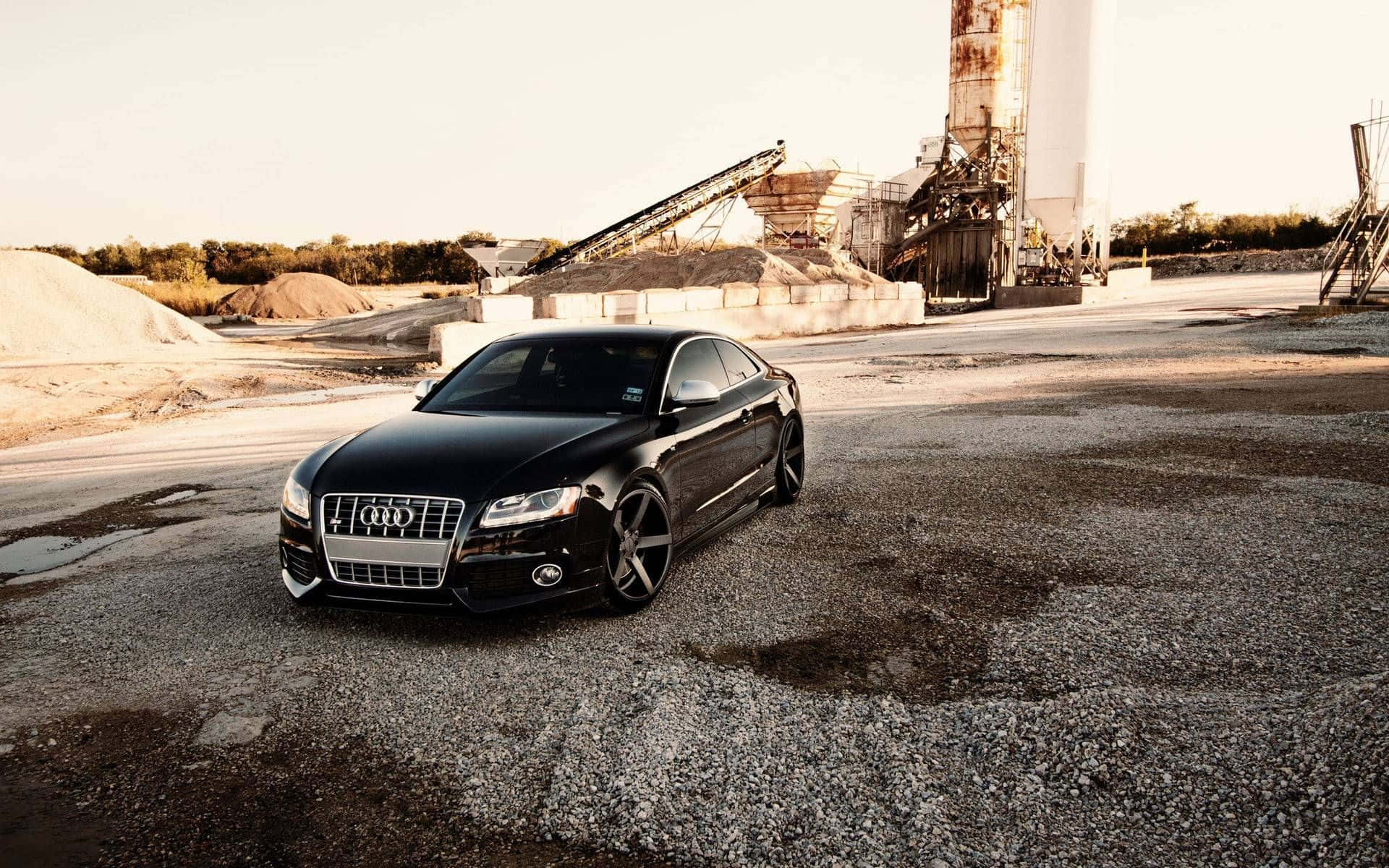 Audi S5 桌布 壁紙 — 一輛時尚黑色奧迪房車停泊在工業採石場的碎石上，正值黃金時刻。