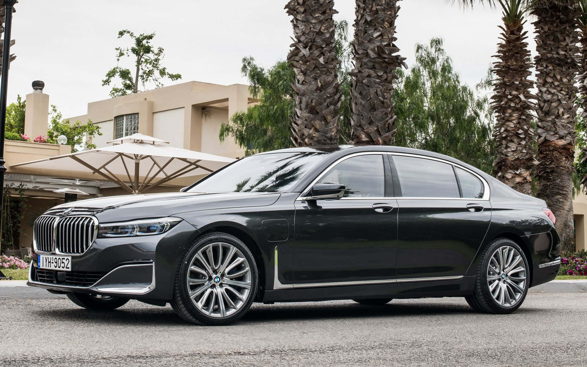 Bmw 7 Series 桌布 壁紙 — 一輛時尚黑色寶馬7系列轎車停放在鋪砌車道上，旁邊有棕櫚樹和現代米色房屋。