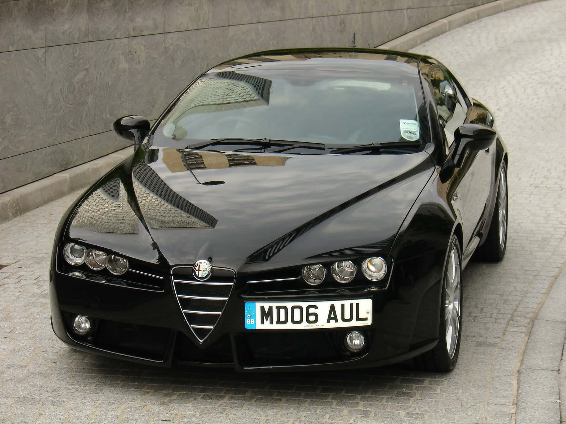 Alfa Romeo Brera 桌布 壁紙 — 一輛時尚黑色愛快羅密歐跑車停放在石牆旁的鵝卵石街道上。