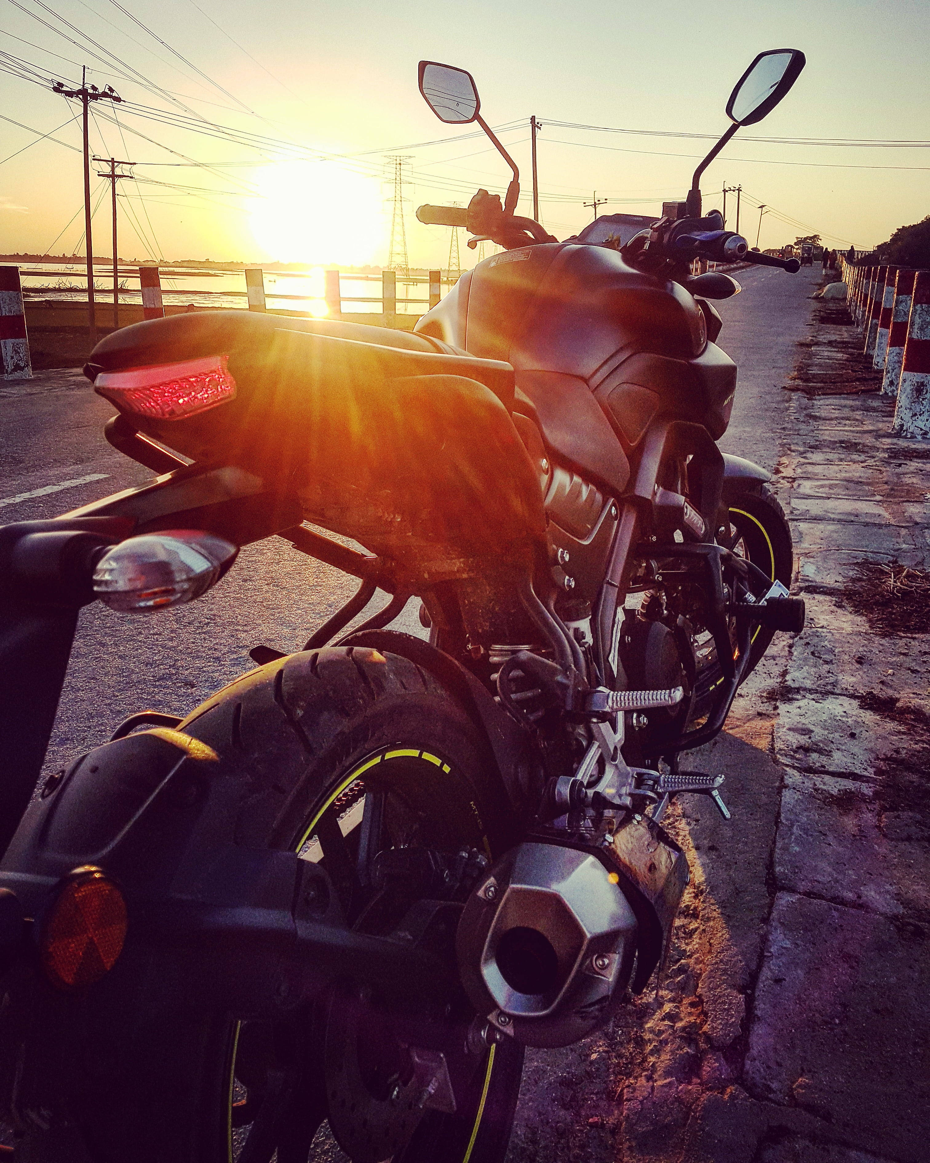 yamaha mt 15 桌布 壁紙 — 一輛時尚黑色機車停放在日落時分的路邊，背後有金色光芒綻放。