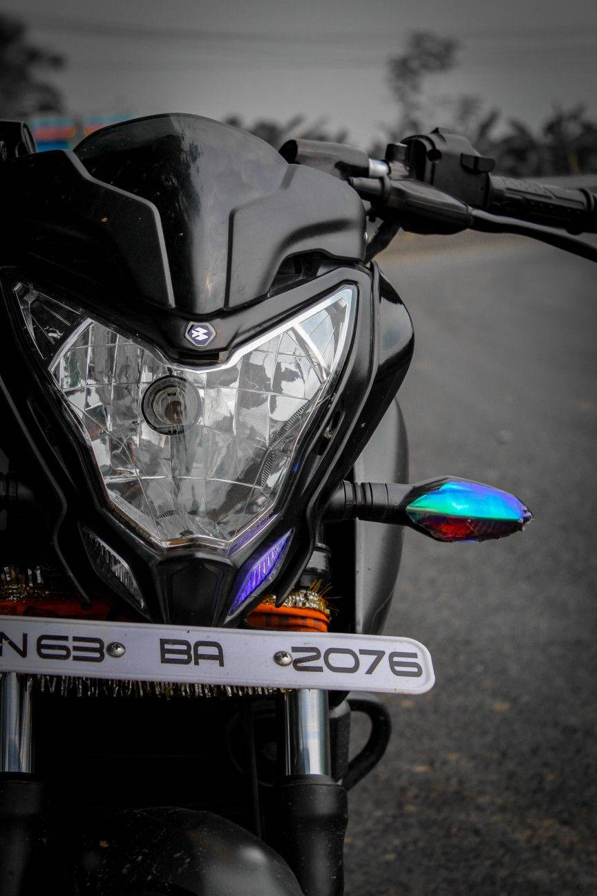機車 桌布 壁紙 — 一輛時尚黑色機車前部的特寫，帶有彩虹色方向燈和鍍鉻前叉，背景是模糊的道路。