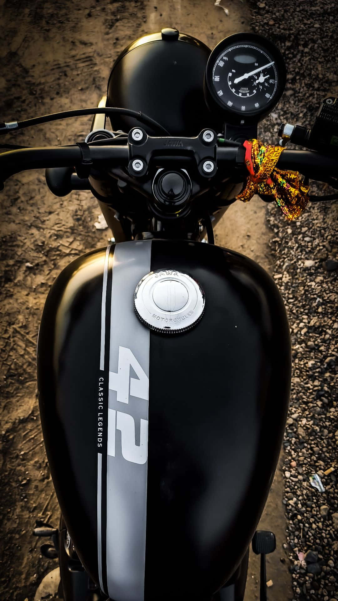  壁紙 — 一輛時尚黑色機車的特寫，油箱上印有「42」和「CLASSIC LEGENDS」，停在碎石地上，把手掛著色彩繽紛的頭巾。