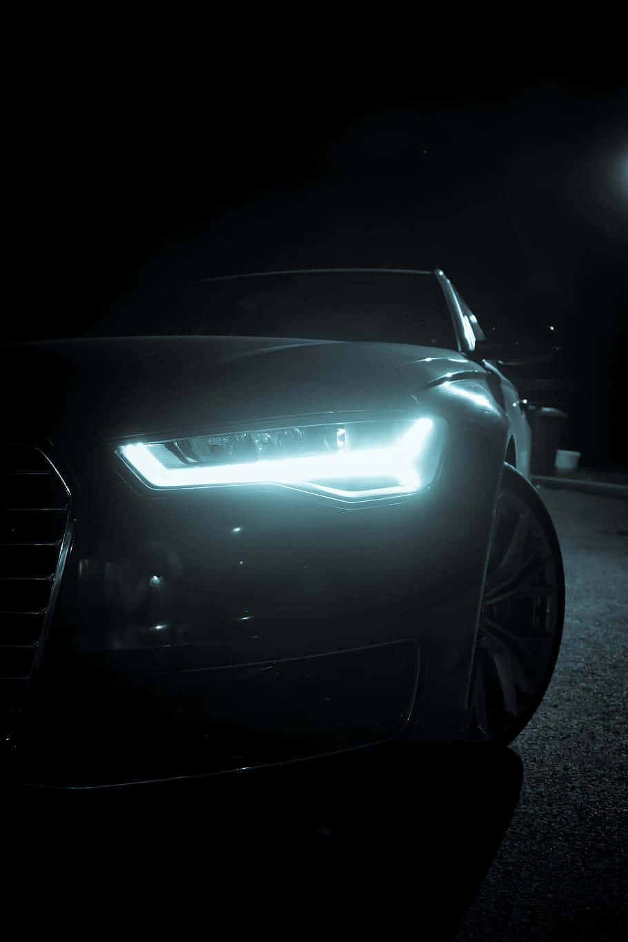 Audi A6 桌布 壁紙 — 一輛時尚黑色汽車的發光車頭燈在夜間城市環境中刺穿黑暗。