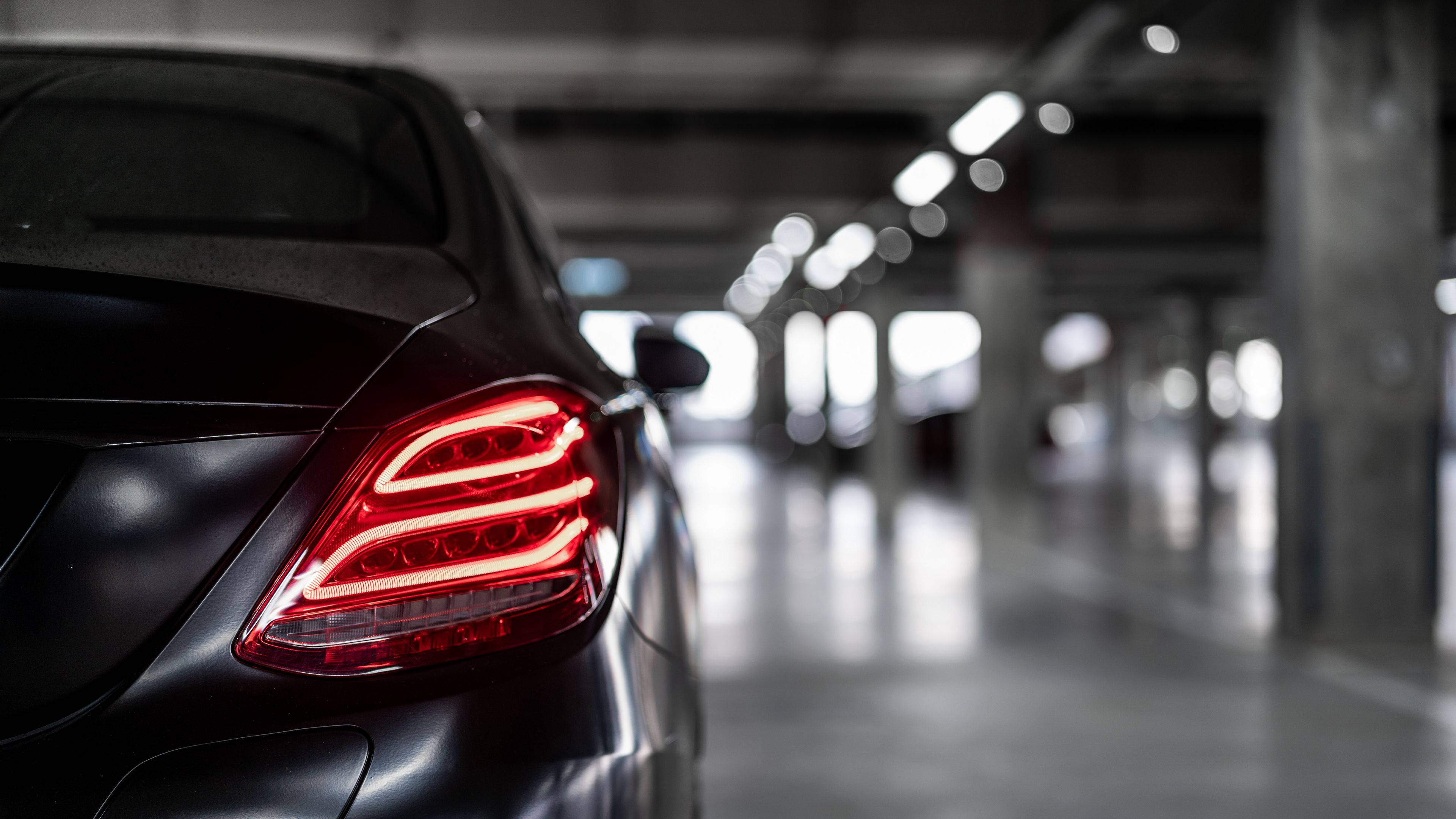 Mercedes 桌布 壁紙 — 一輛時尚黑色汽車的紅色尾燈在光線昏暗的地下停車場中格外醒目。