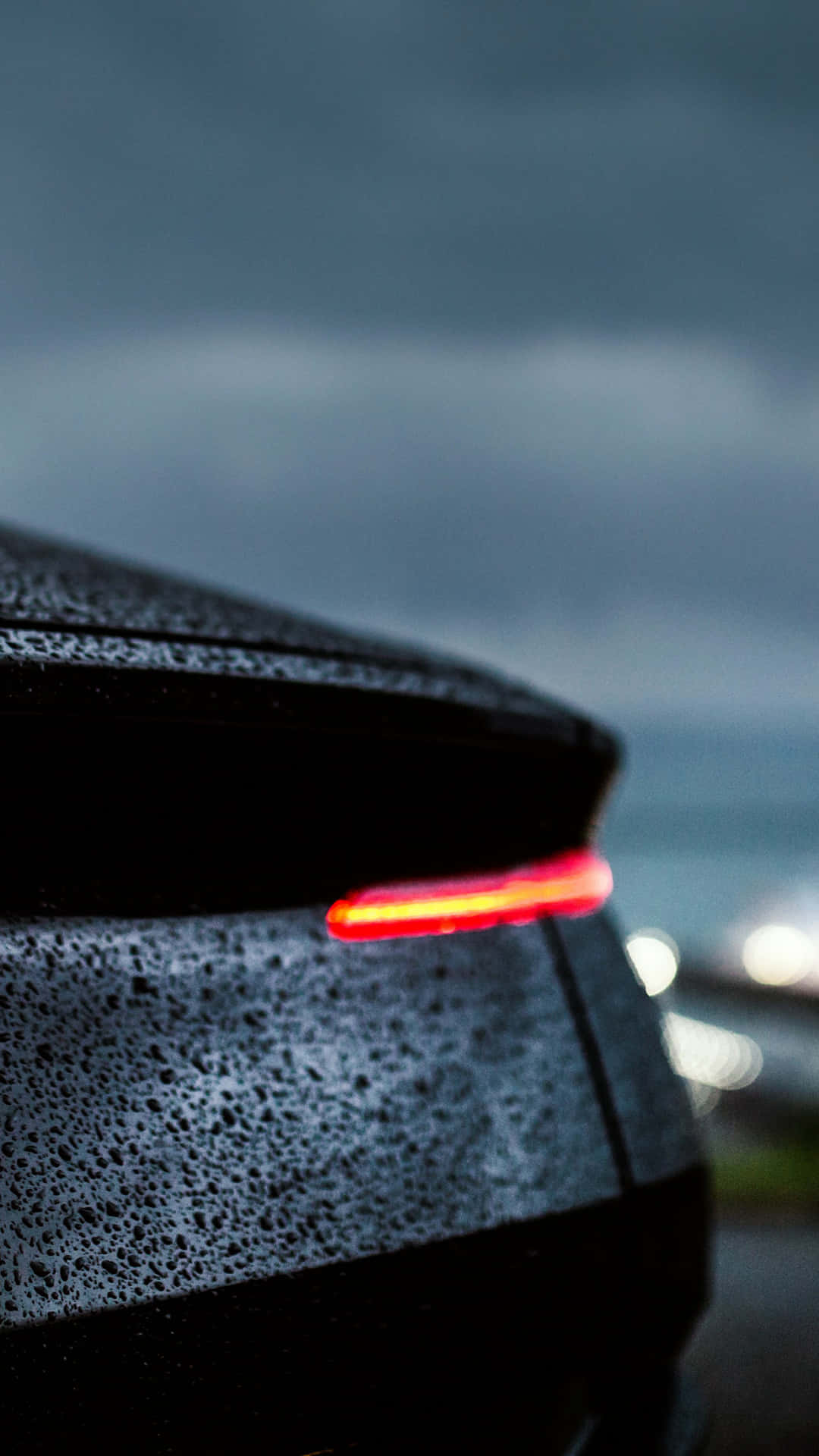 Rain 4K 桌布 壁紙 — 一輛時尚黑色汽車的紅色尾燈在雨中黃昏的天空中閃耀，遠處的城市燈光模糊不清。