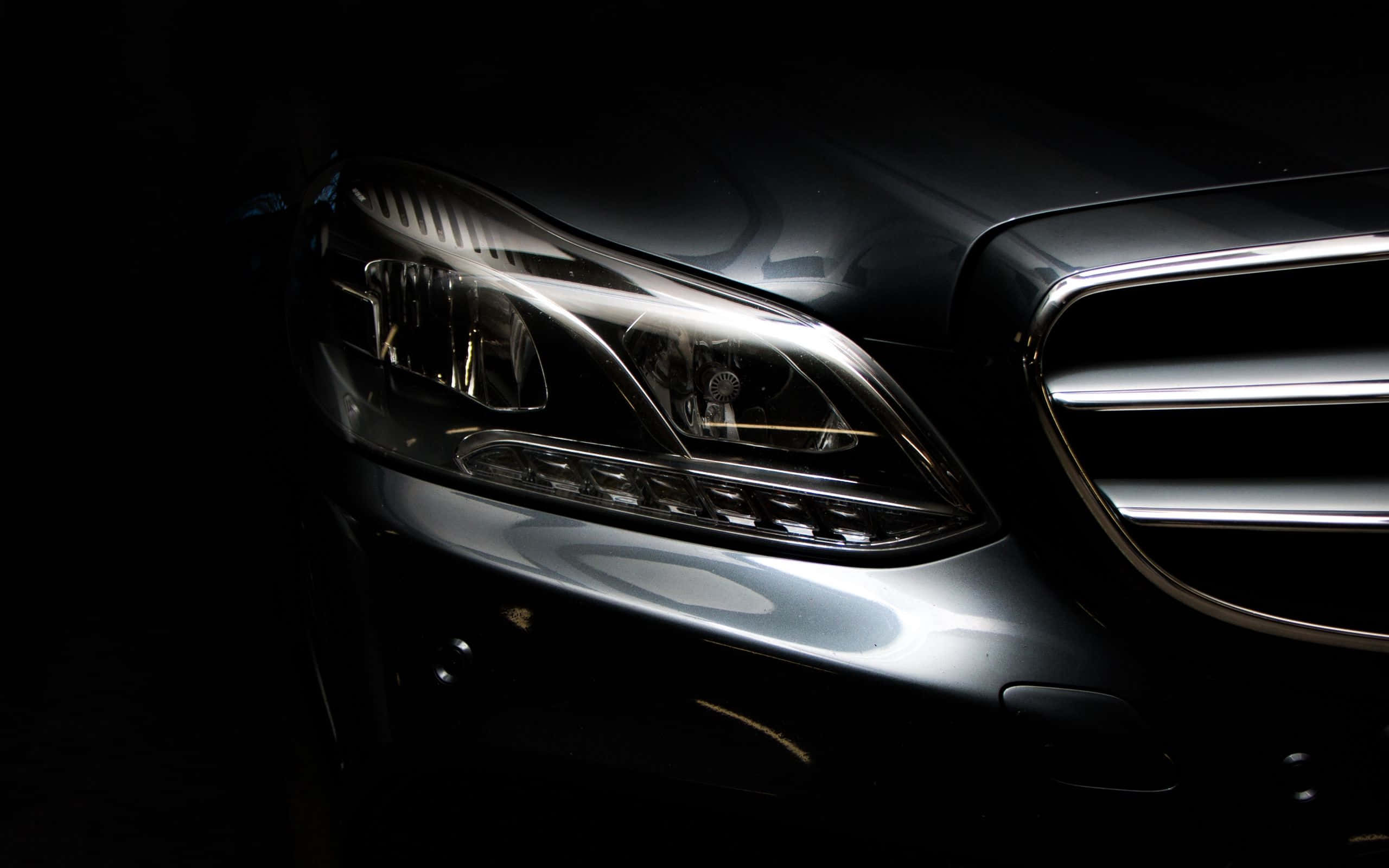 Mercedes 桌布 壁紙 — 一輛時尚黑色汽車的車頭燈在漆黑背景下發出銳利光芒，突顯其拋光鍍鉻格柵和空氣動力學曲線。