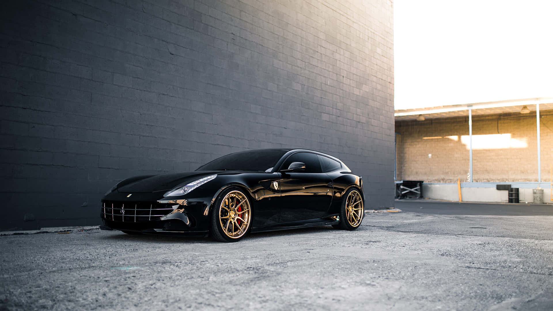 Ferrari Ff 桌布 壁紙 — 一輛時尚黑色法拉利配金色輪圈，停泊在都市地塊的深灰色磚牆旁。