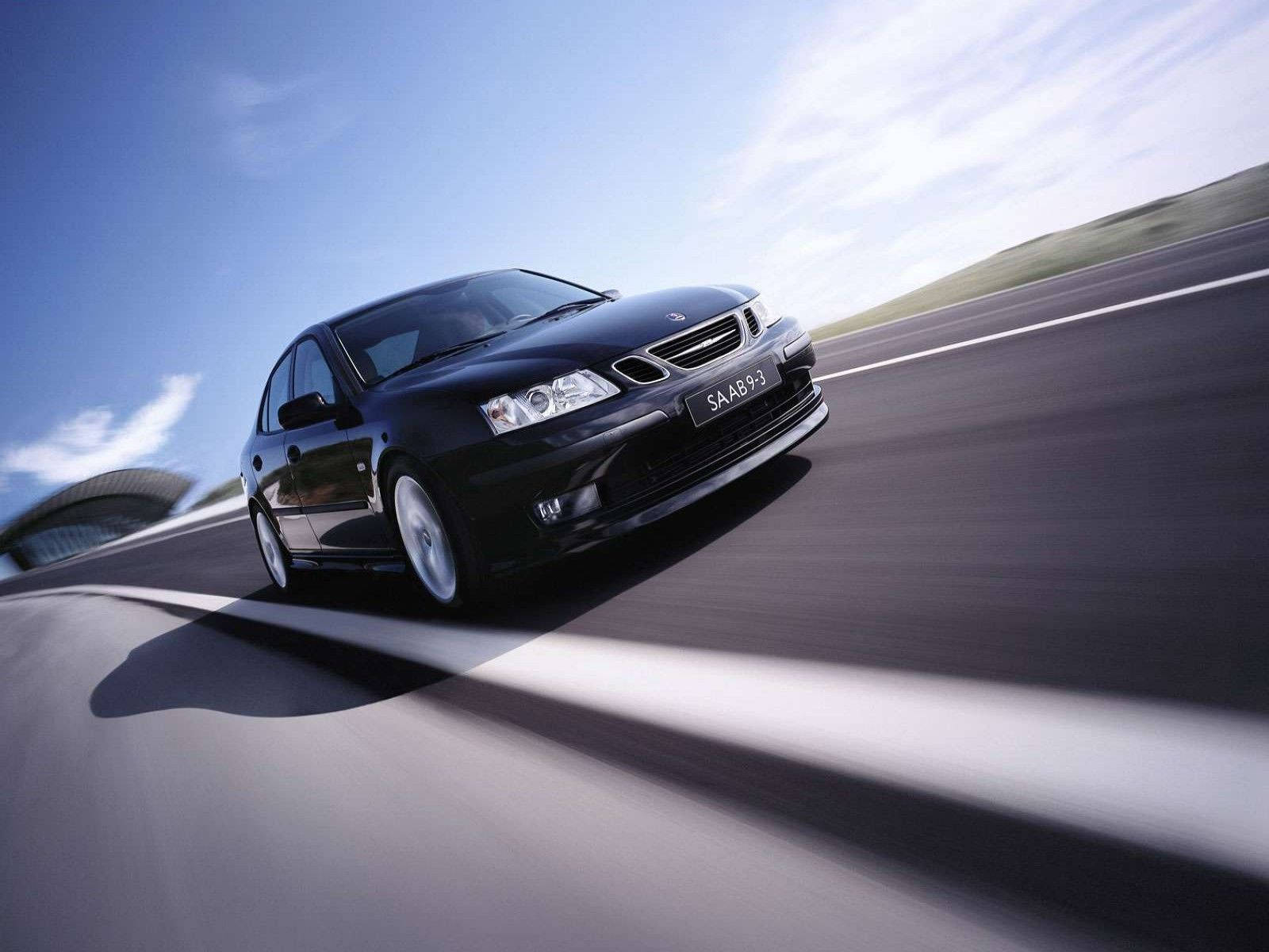 Saab 桌布 壁紙 — 一輛時尚黑色薩博9-3在明亮藍天下沿著彎曲賽道疾馳，動態模糊強調速度。