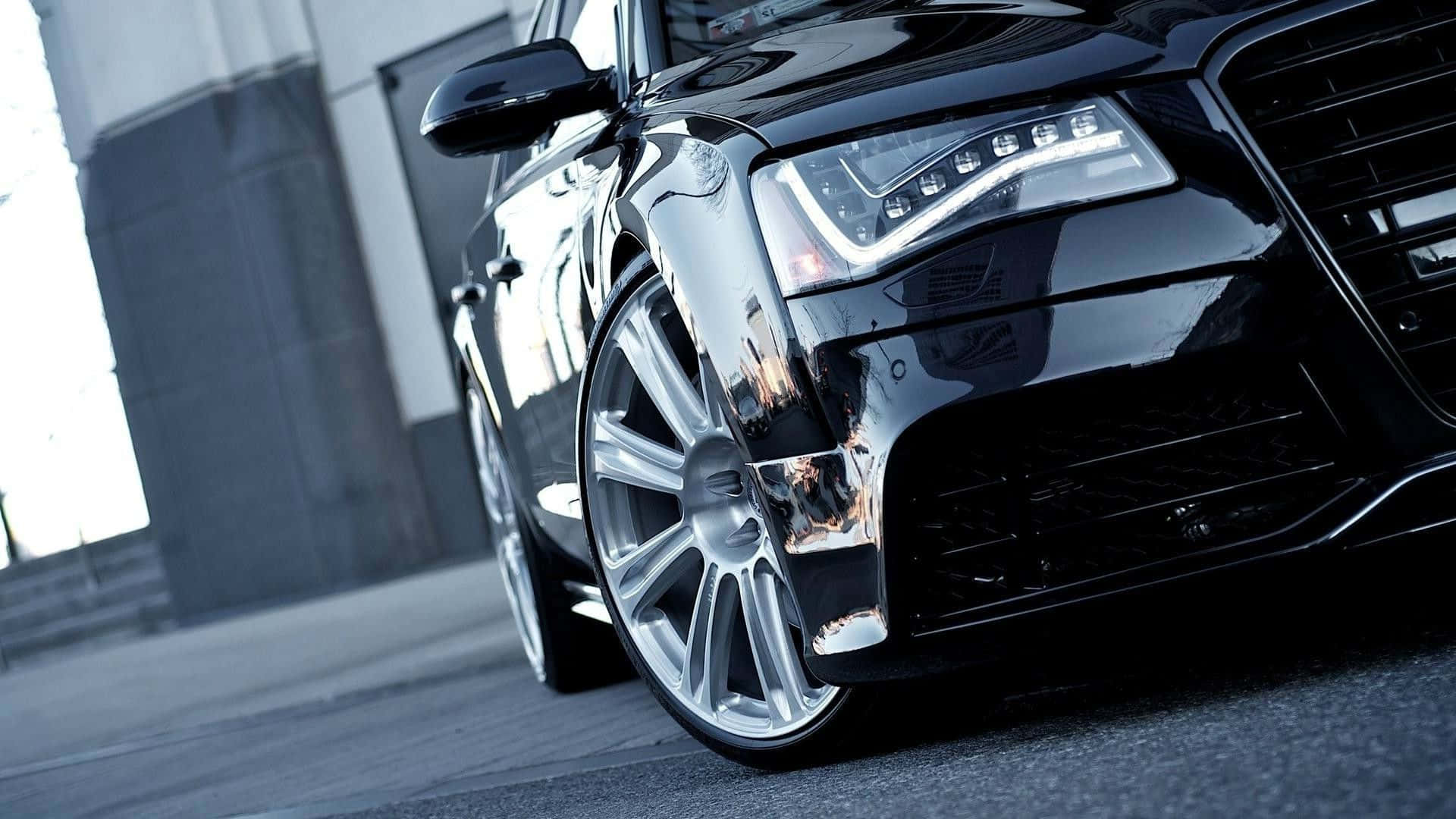 Audi S8 桌布 壁紙 — 一輛時尚黑色豪華轎車的前輪和頭燈在都市日光下閃耀，帶有反光鍍鉻裝飾。