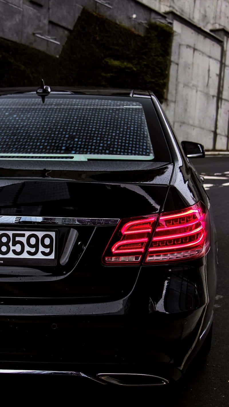 Black Car 桌布 壁紙 — 一輛時尚黑色豪華轎車的發光紅色尾燈反射在潮濕的路面上，旁邊是長滿青苔的混凝土牆。