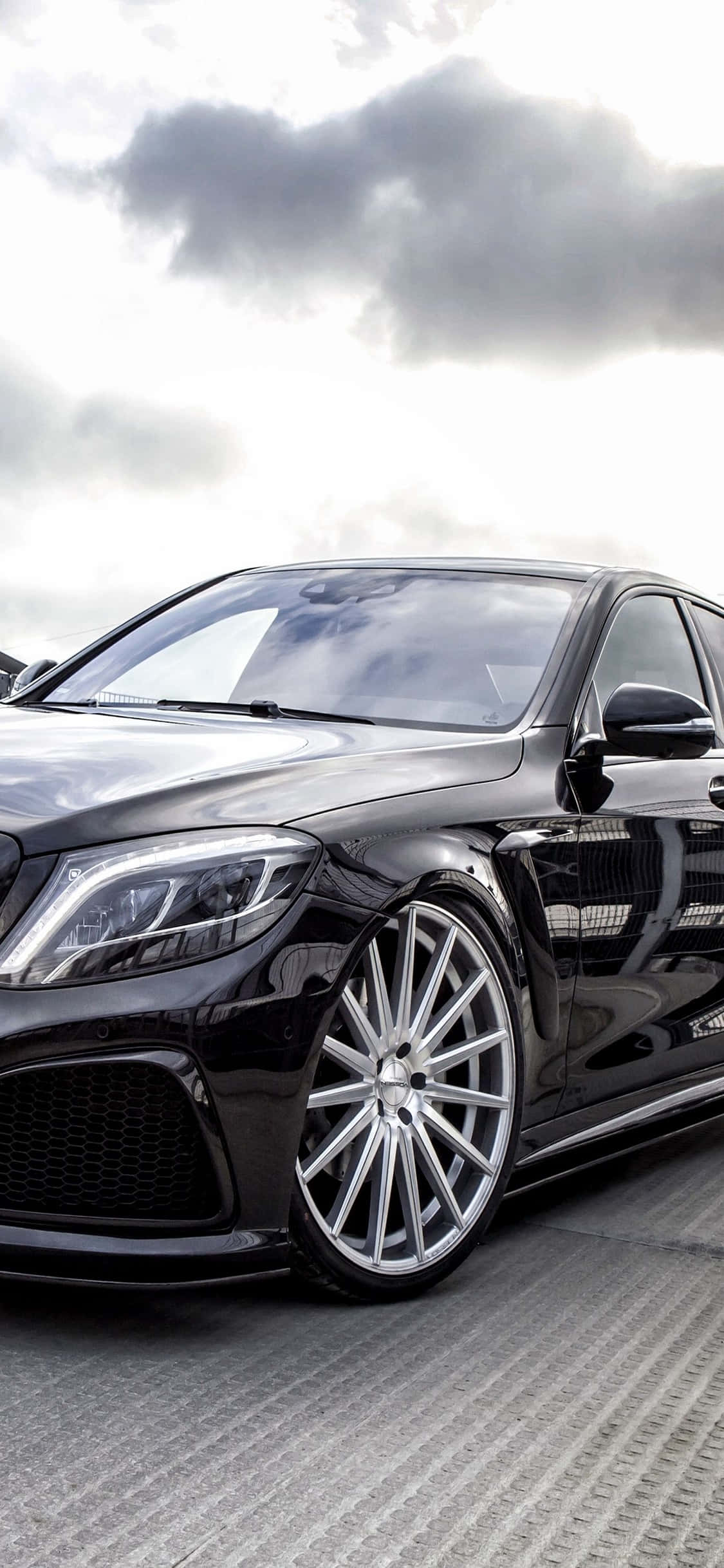 Mercedes 桌布 壁紙 — 一輛時尚黑色豪華轎車配銀色輪圈，停泊在紋理路面，天空多雲。