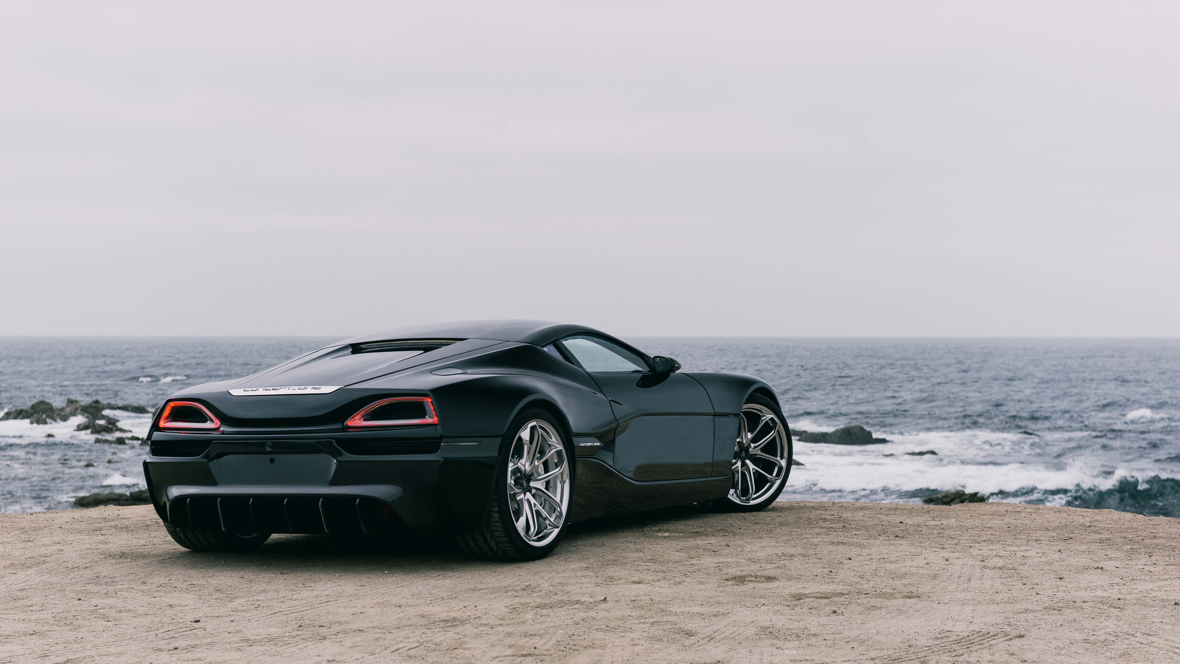 Rimac 桌布 壁紙 — 一輛時尚黑色跑車停泊在崎嶇懸崖上，俯瞰著陰天下的暴風雨海洋。