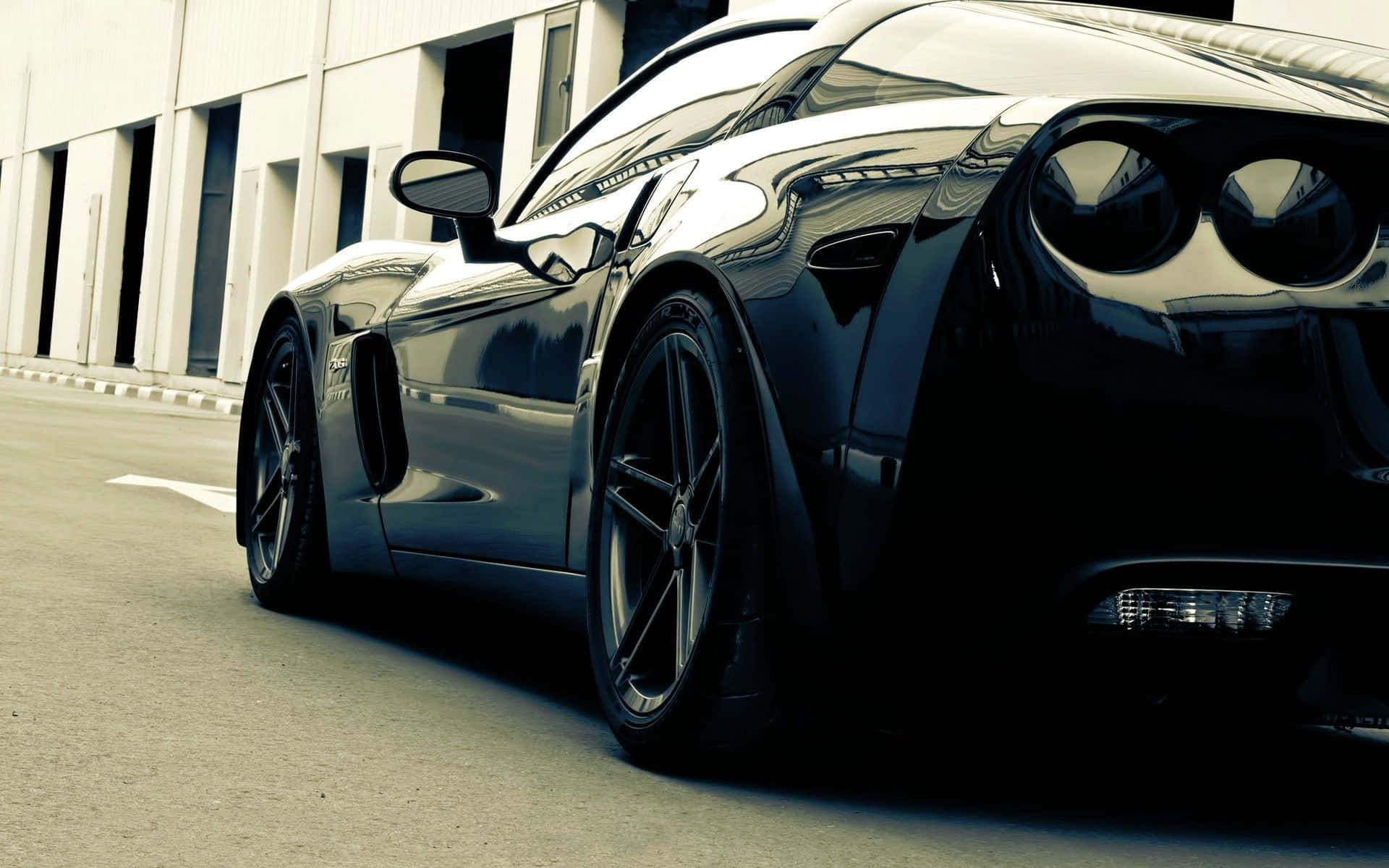Chevrolet Corvette Z06 桌布 壁紙 — 一輛時尚黑色跑車在強光下閃耀，拋光表面反射光線，停泊在現代建築旁。
