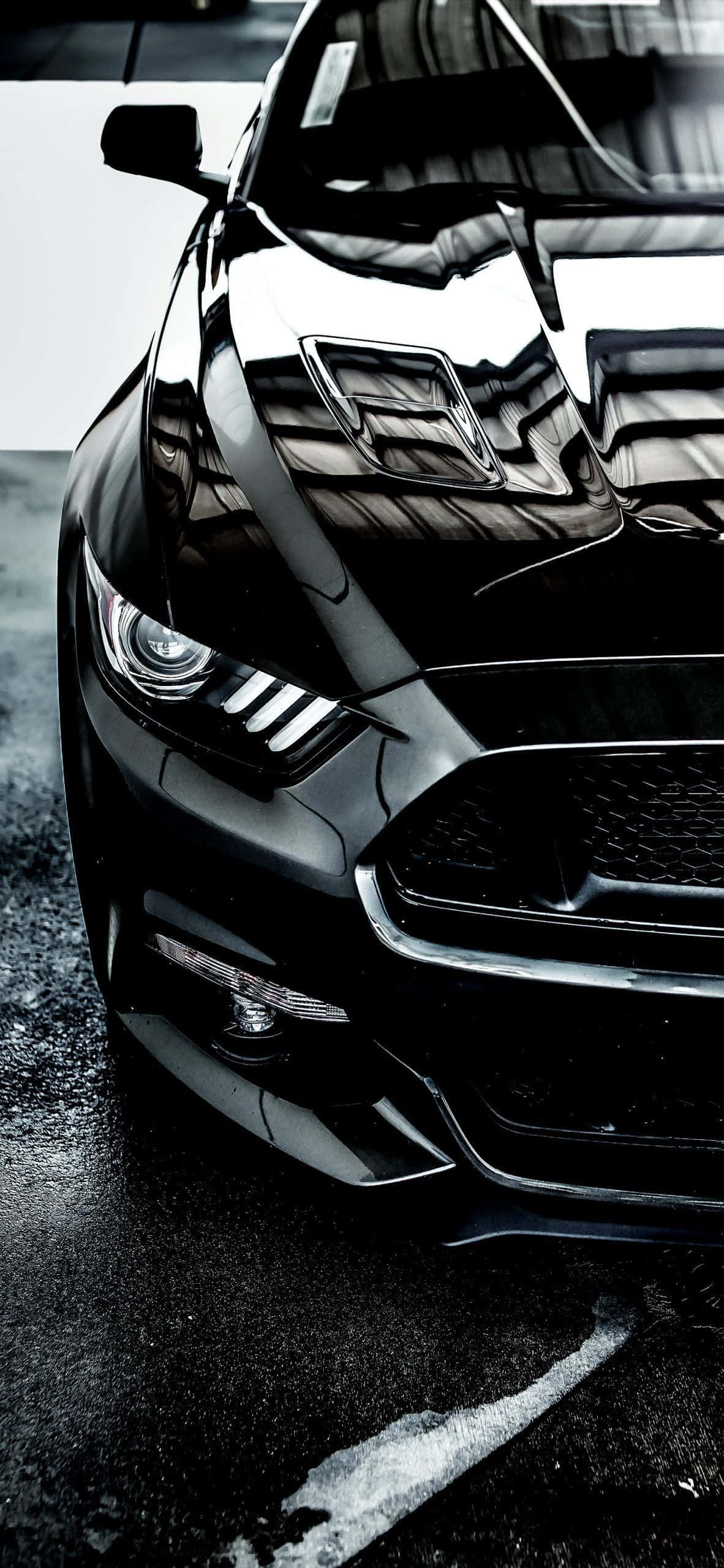 Mustang iPhone 桌布 壁紙 — 一輛時尚黑色跑車在戲劇性燈光下閃耀，濕漉漉的路面反射出其銳利線條和鍍鉻裝飾。