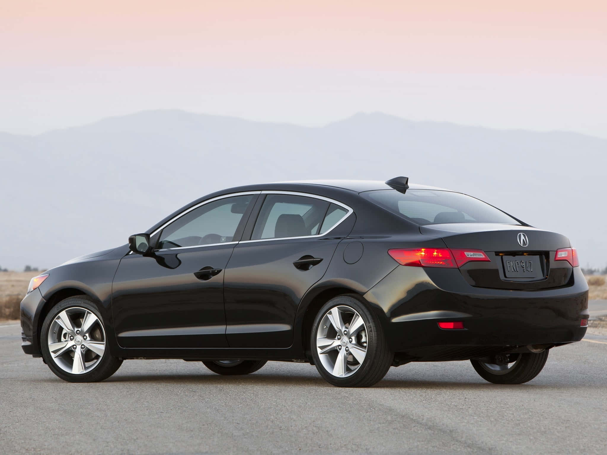 Acura Ilx 桌布 壁紙 — 一輛時尚黑色轎車停泊在鋪砌道路上，遠山在柔和粉紅與橙色夕陽天空下。