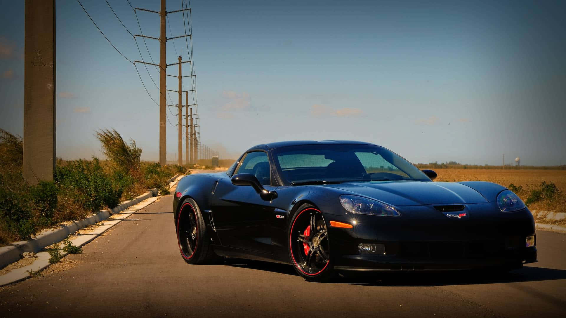 Chevrolet Corvette Z06 桌布 壁紙 — 一輛時尚黑色雪佛蘭Corvette，配紅色輪圈，停泊在沙漠公路上，天空湛藍。