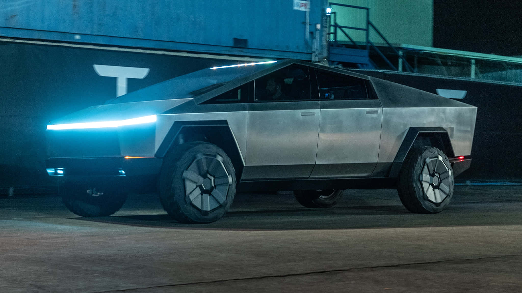 Cybertruck 桌布 壁紙 — 一輛未來感十足的銀色 Tesla Cybertruck 在夜間昏暗的工業車庫中，在霓虹藍色頭燈下閃閃發光。