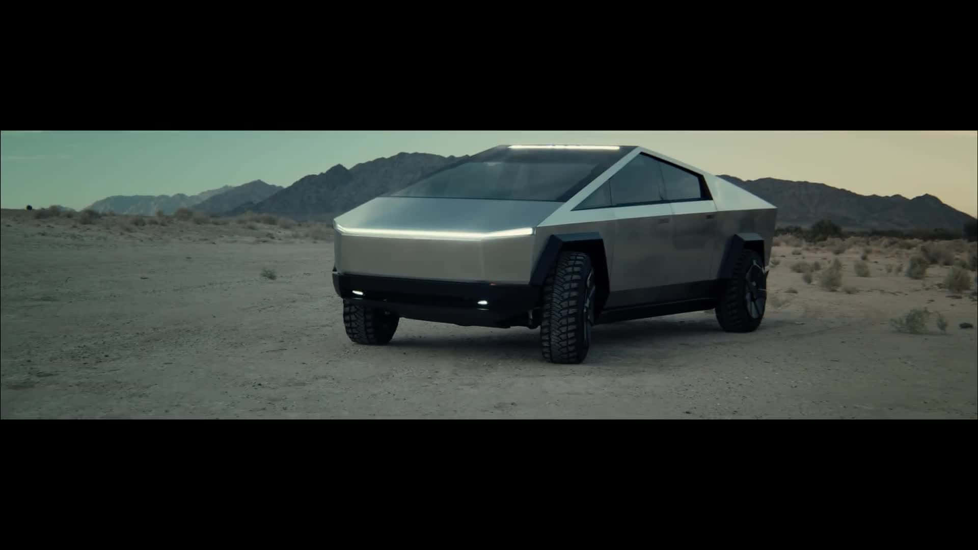 Tesla Cybertruck 桌布 壁紙 — 一輛未來感十足的銀色 Tesla Cybertruck 孤獨地矗立在荒蕪的沙漠中，遠山在暗淡的天空下若隱若現。