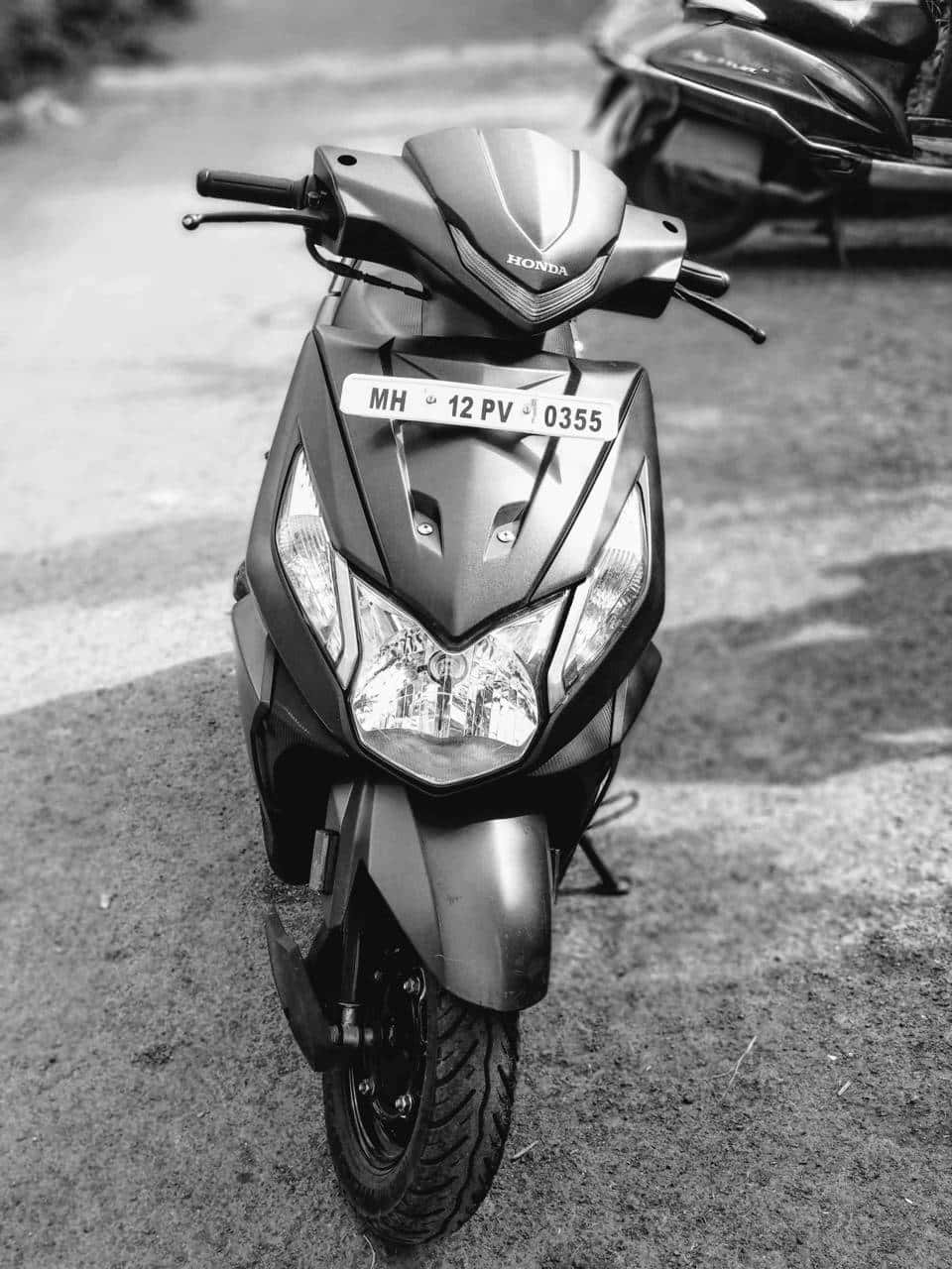 grayscale 桌布 壁紙 — 一輛本田機車停放在鋪砌路面上的黑白特寫，背景有另一輛機車模糊不清。